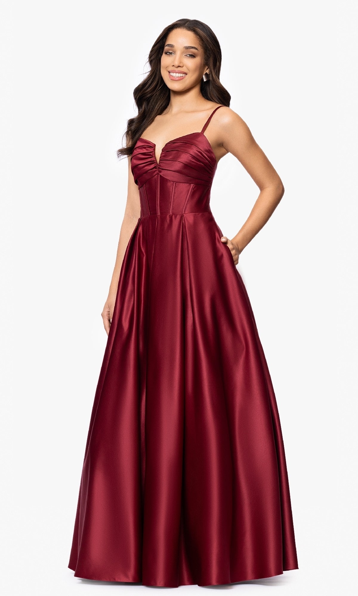 A woman wears the Blondie Nites 5207BN long prom dress—sleeveless, deep red satin with a fitted corset bodice and thin straps—standing against a plain white background.