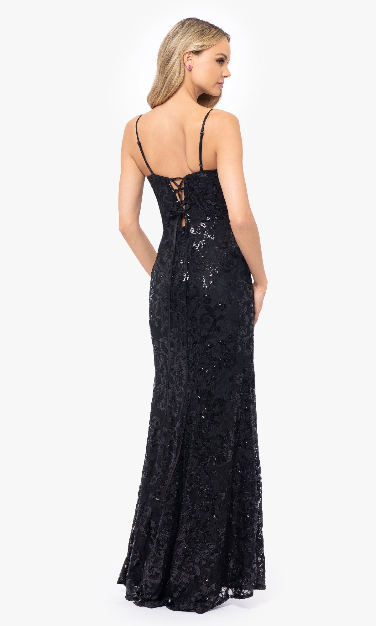 A woman stands facing away in the Blondie Nites 5213BN Black Sequin-Print Prom Dress, featuring a floor-length design with thin straps, a sheer corset bodice, and a lace-up back.