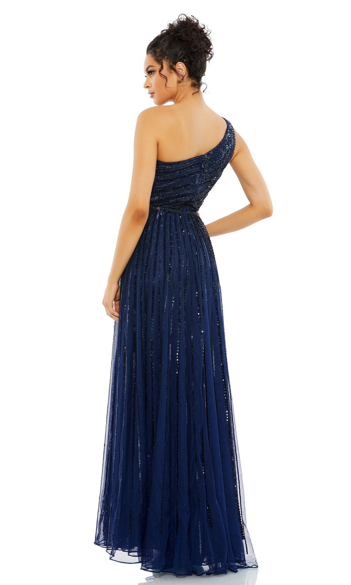 A woman faces away in the Mac Duggal 5220 One-Shoulder Beaded Formal Dress, a navy blue A-line evening gown featuring a fitted bodice, flowing skirt, and subtle sequin embellishments.