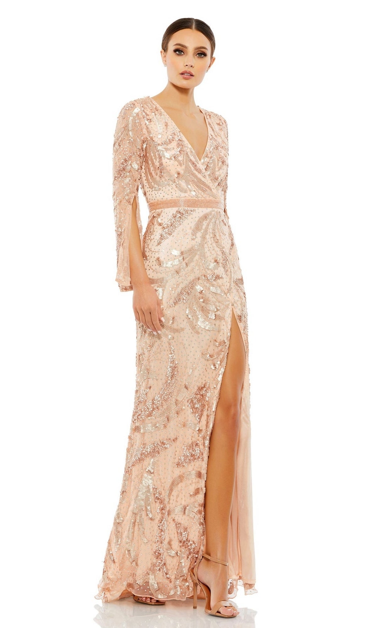 A woman in the Long Formal Dress 5222 by Mac Duggal, featuring blush pink beading, long sleeves, a V-neckline, and a thigh-high slit, styled with nude high-heeled sandals.