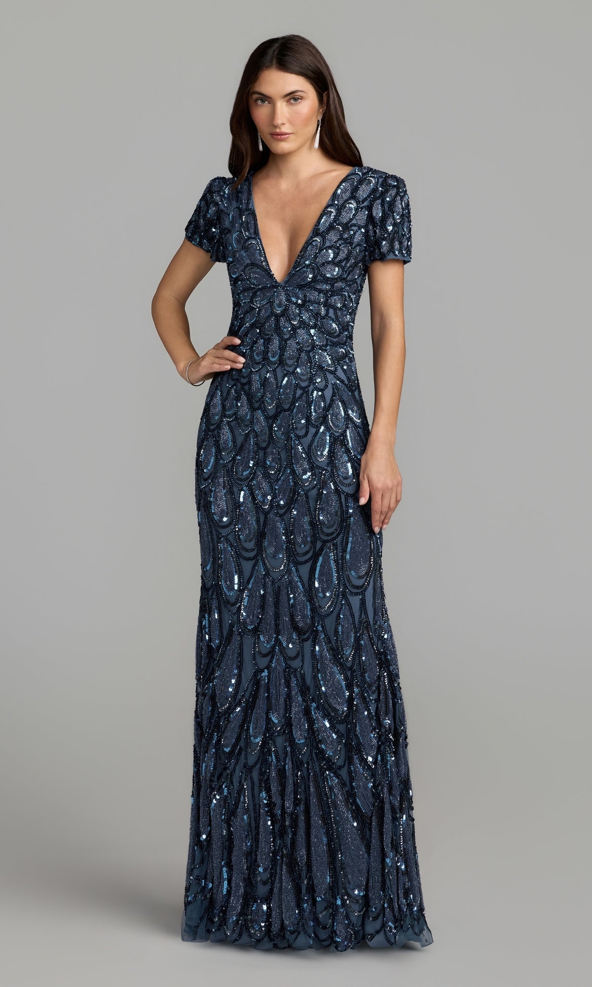 A woman wearing the Mac Duggal 5243 Sequin Long Formal Dress in denim, a floor-length gown with short sleeves and a deep V-neckline, featuring an intricate sequin pattern, stands against a plain background.