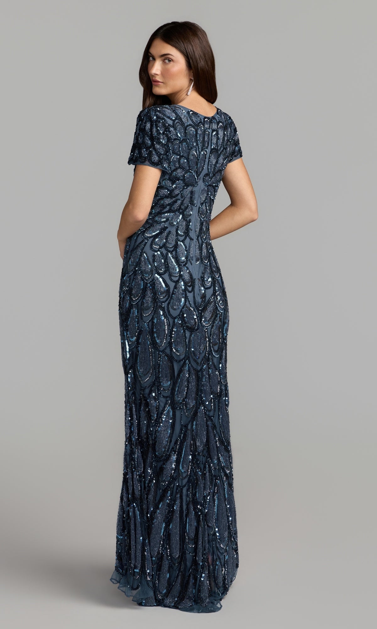 Woman in a floor-length, brown Mac Duggal 5243 sequin long formal dress with short sleeves, standing and facing away to showcase the back detail of the gown against a plain background.