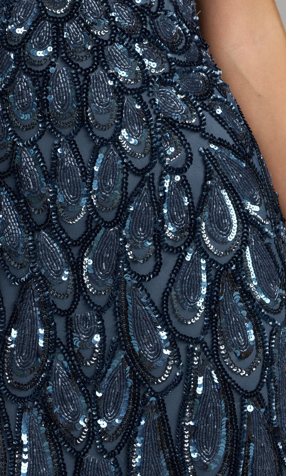 Close-up of dark blue fabric adorned with sequins and bead embellishments in a teardrop pattern, echoing the intricate detailing featured on the Sequin Long Brown Formal Dress: Mac Duggal 5243; a person’s arm is visible on the right.
