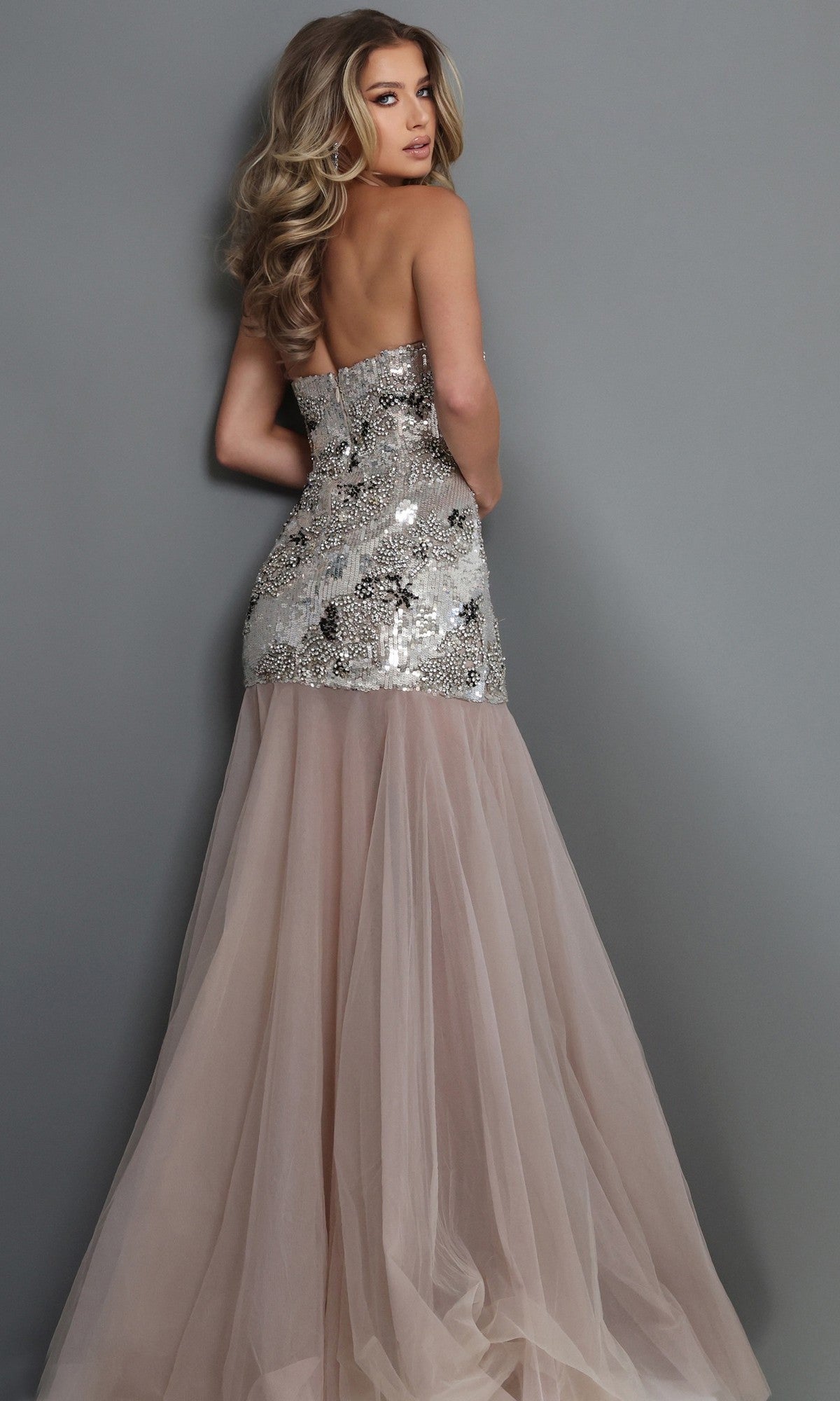 Model faces away, wearing the Jovani 52538 long formal dress, featuring a strapless sequined bodice embellished with delicate crystal beadwork and a flowing blush tulle skirt, set against a plain gray background.