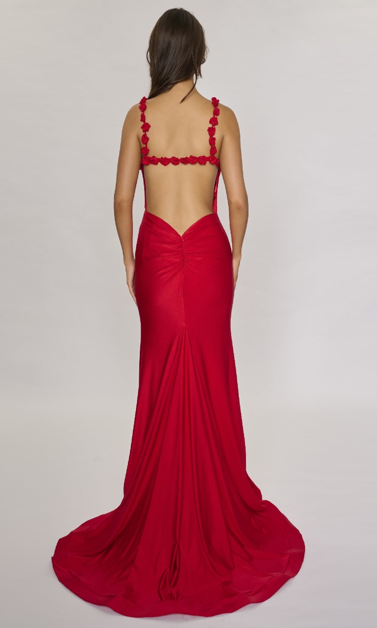 A woman models the Nina Canacci 5304, a floor-length formal dress featuring a backless design and 3D rose accents on the straps, against a plain light background.