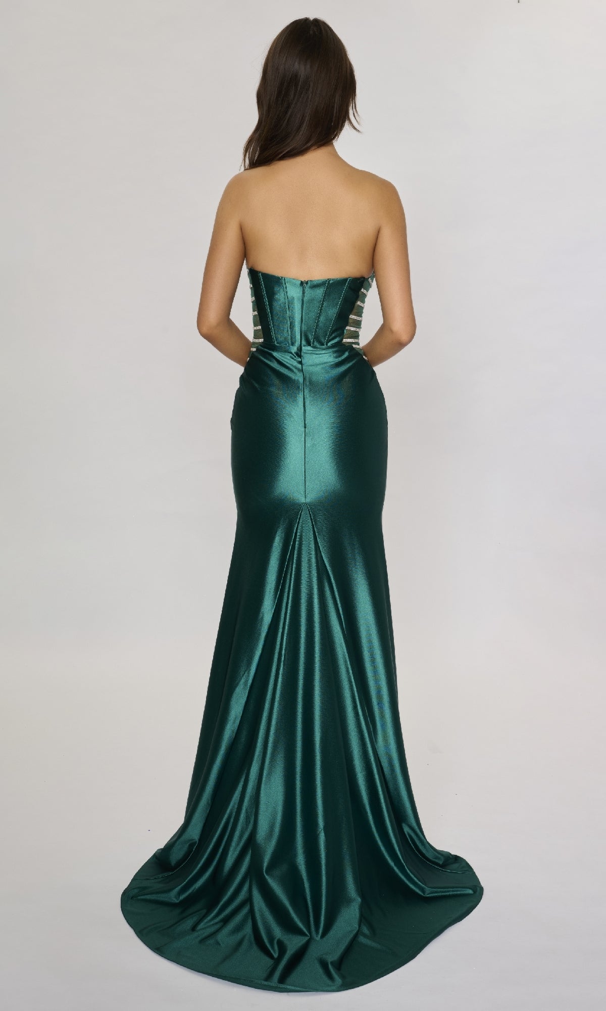 A woman faces away, wearing the Nina Canacci 5307 long formal dress—an emerald green, strapless satin gown with a fitted bodice and flared, trailing skirt.