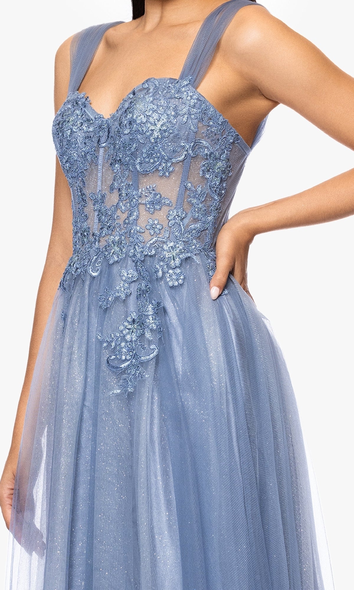 A person wearing the Blondie Nites 5311BN long prom dress, which features a sleeveless light blue design with a corset bodice, floral embroidery, sheer straps, and delicate lace and tulle fabric.