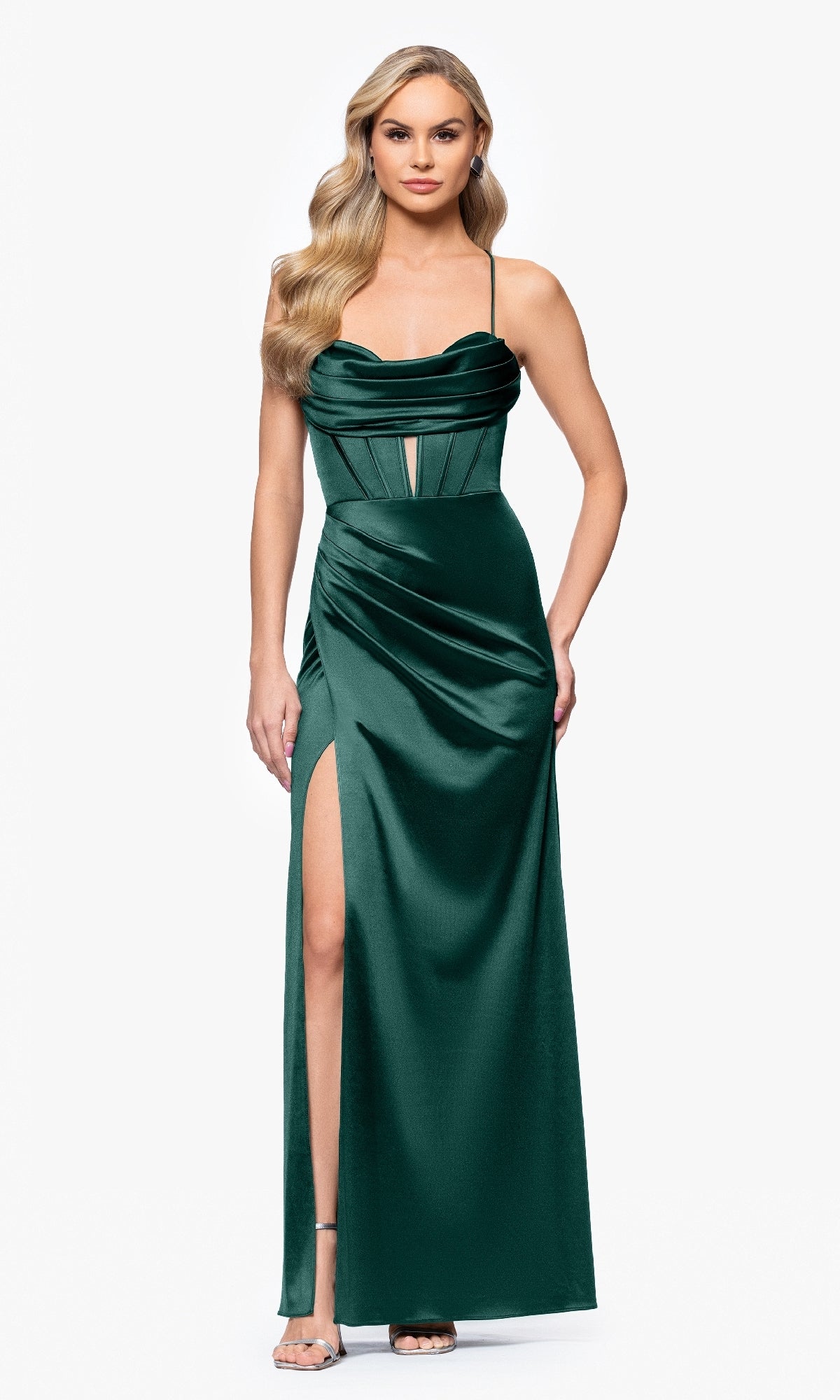 A woman wears the Long Dark Green Prom Dress: Blondie Nites 5319BN, featuring a sleeveless, floor-length design with a thigh-high slit, thin straps, and a corset bodice. She stands against a plain white background.