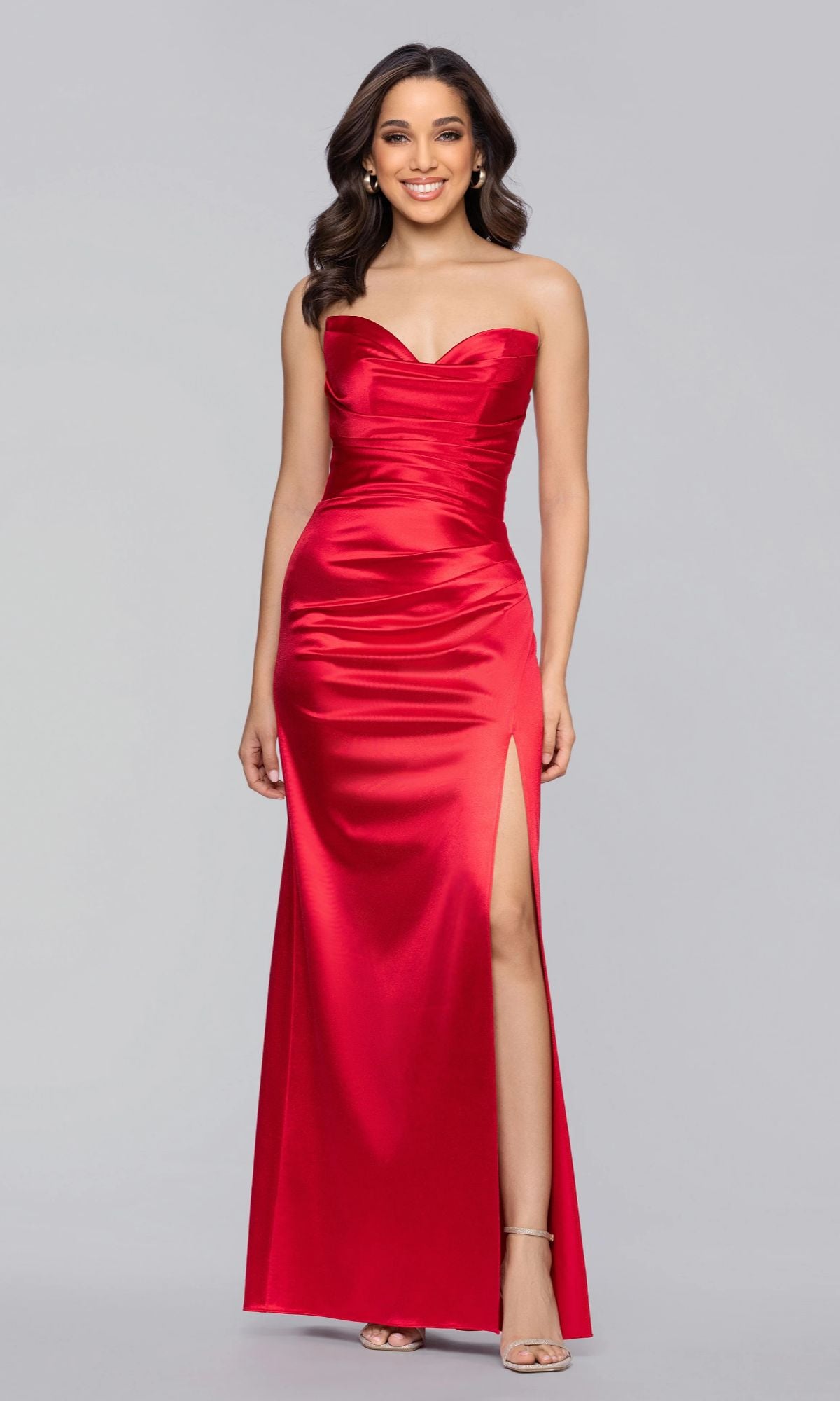 A woman stands against a plain gray background wearing the Blondie Nites 5355BN Long Prom Dress in red, a strapless satin gown with a sweetheart neckline and dramatic leg slit.