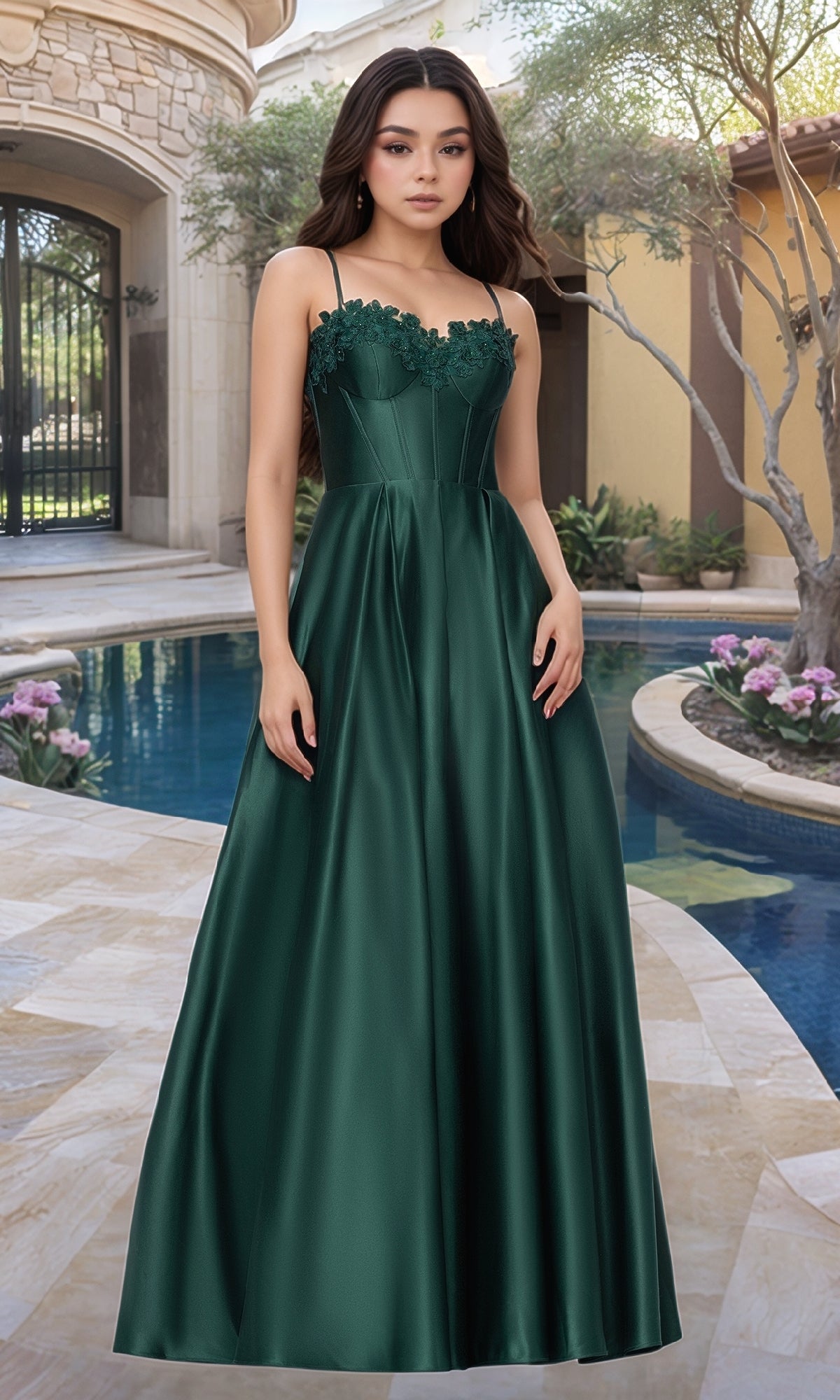 A woman stands on a stone patio by a pool, wearing the Blondie Nites 5387BN Classic Long Prom Dress in Hunter, featuring an embroidered-lace corset, with landscaped plants and a building in the background.