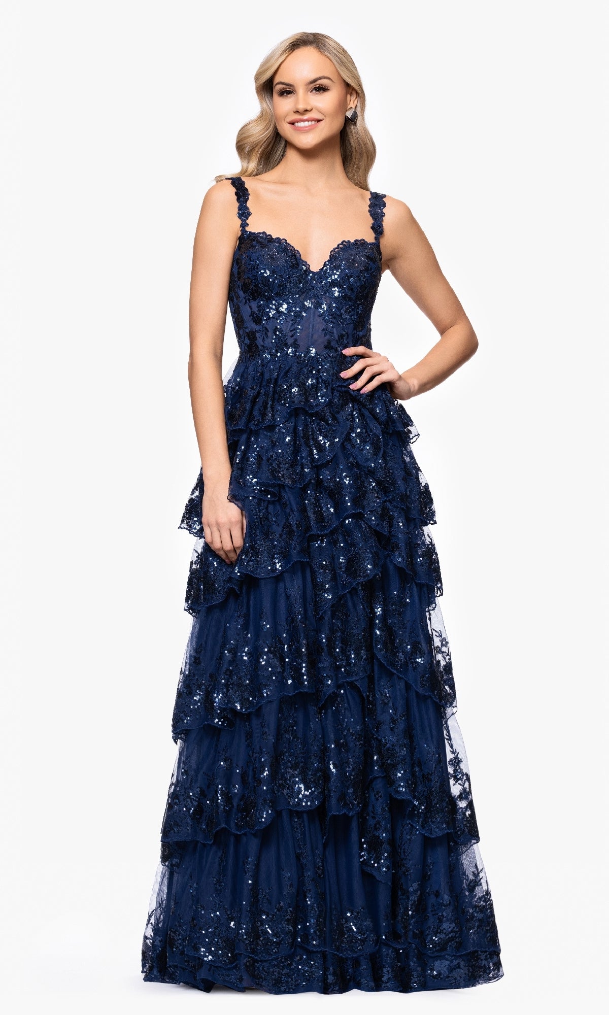 A woman stands against a white background wearing the Long Navy Prom Dress Blondie Nites 5394BN, which features sequin embellishments, lace appliques, a sleeveless design, and a tiered A-line skirt.