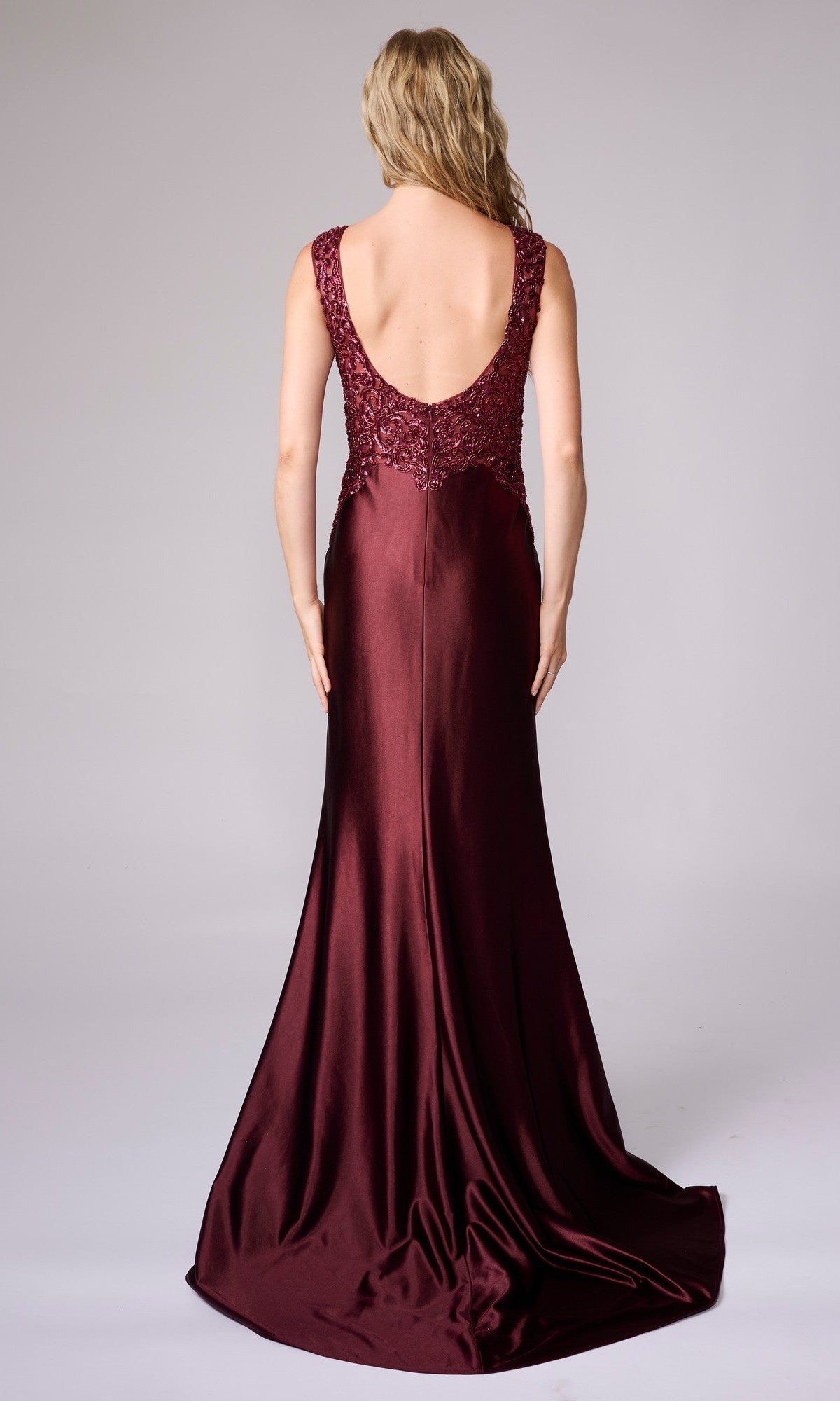 A woman with wavy blonde hair wears the Nina Canacci 5411, a sleeveless, floor-length formal dress with a low back and lace details, posing against a plain background.