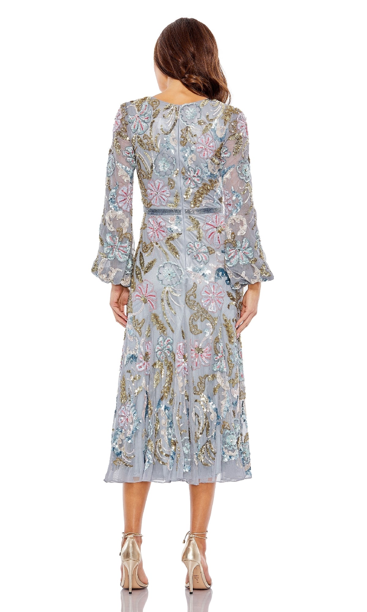 A woman faces away, wearing the Mac Duggal 5423 Midi Wedding Guest Dress, featuring light blue floral embroidery, beaded accents, long sheer sleeves, and metallic heels—a stunning choice for any wedding guest.