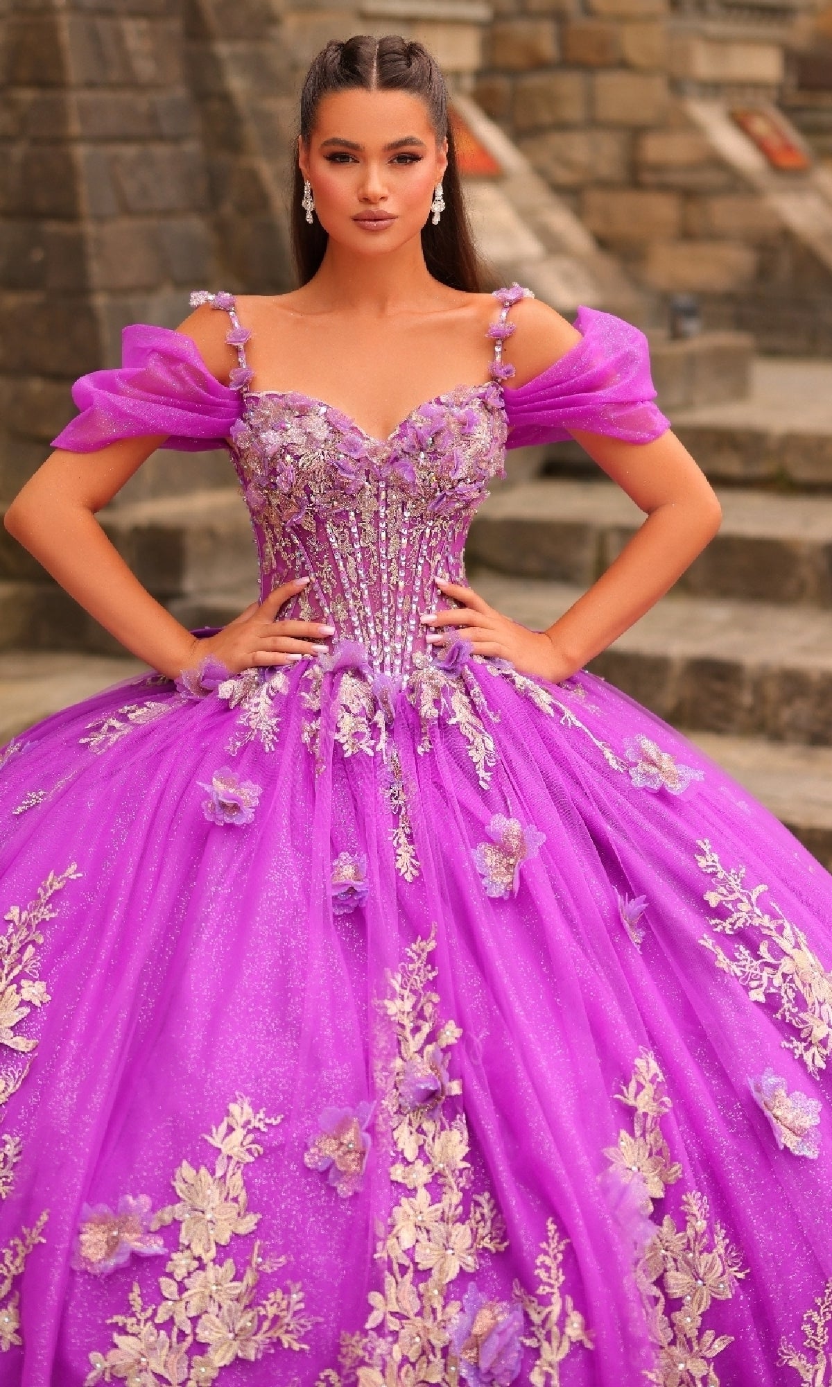A woman stands on stone steps wearing the Amarra 54241 Puff-Sleeve Quinceanera Dress, featuring bright purple fabric with floral embroidery, 3D flowers, and bead details, her hands resting on her hips.