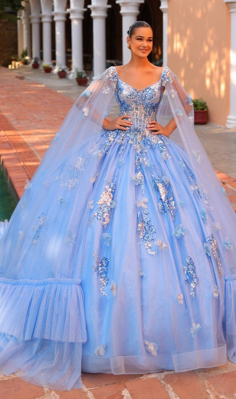 A woman stands outdoors in the Quinceanera Dress 54318 by Amarra, a voluminous light blue ball gown with sparkling embellishments, floral embroidery, and sheer cape sleeves.
