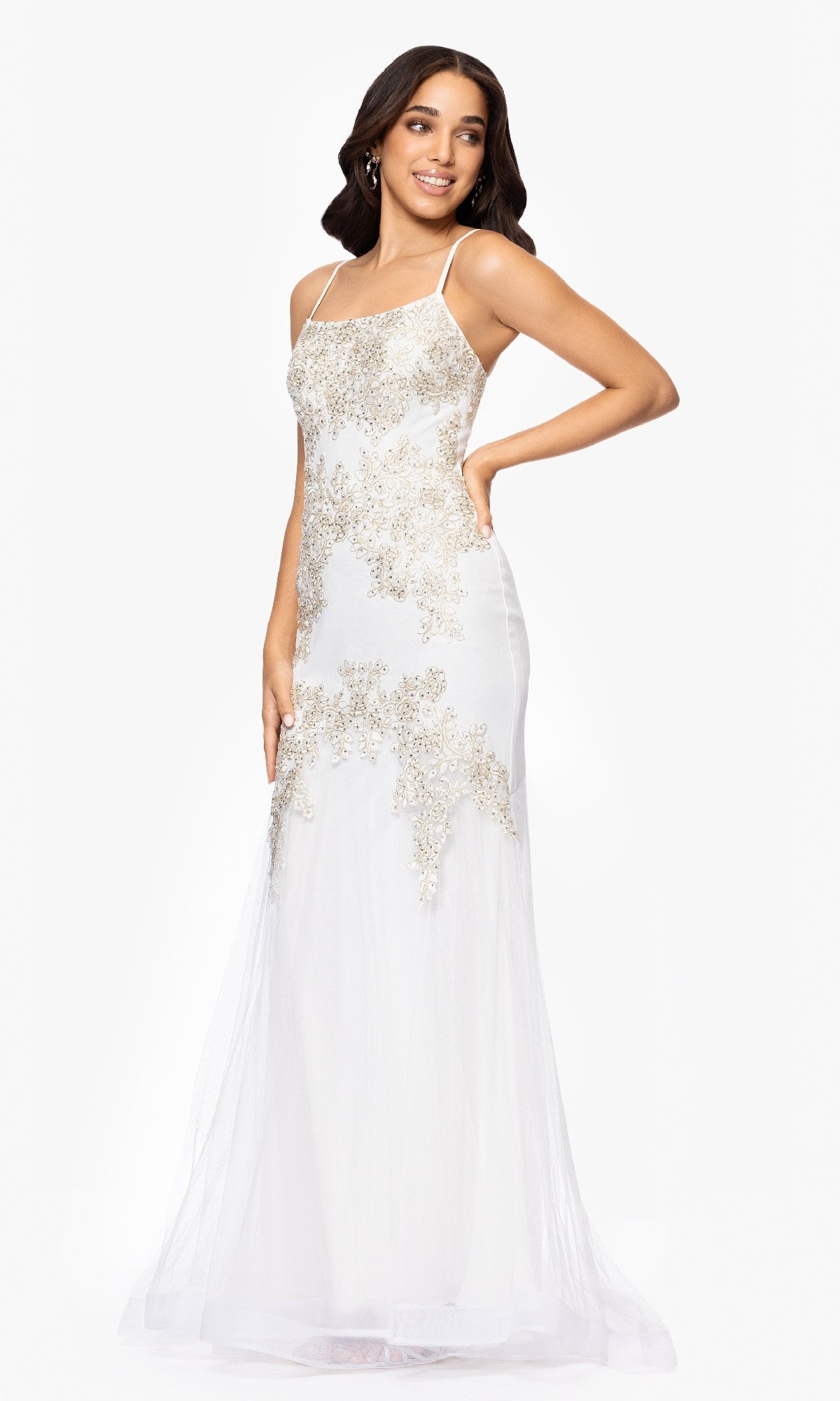 A woman smiles in the Long Prom Dress: Blondie Nites 5455BN, featuring ivory fabric with thin straps and gold lace appliques, standing against a plain white background.