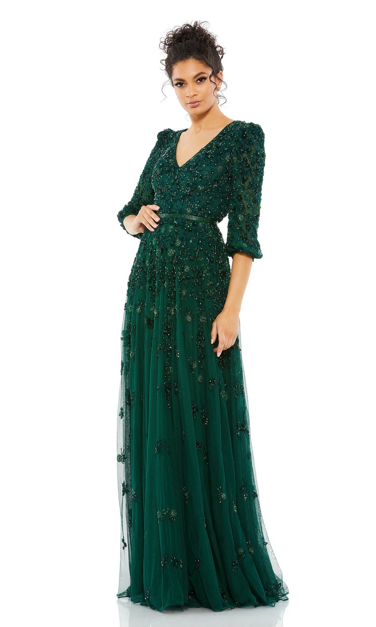 A woman stands against a white background in the Mac Duggal 5497 Long Sleeve Beaded Formal Dress—an emerald green, floor-length gown featuring a V-neckline, three-quarter sleeves, and intricate bead embellishments.