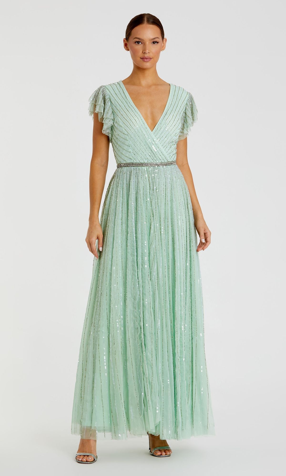 A woman wears the Mac Duggal 5502 Sequin-Stripe Long Formal Dress, featuring a floor-length mint green design with a V-neck, short flutter sleeves, silver waistband, and sparkling sequin accents.