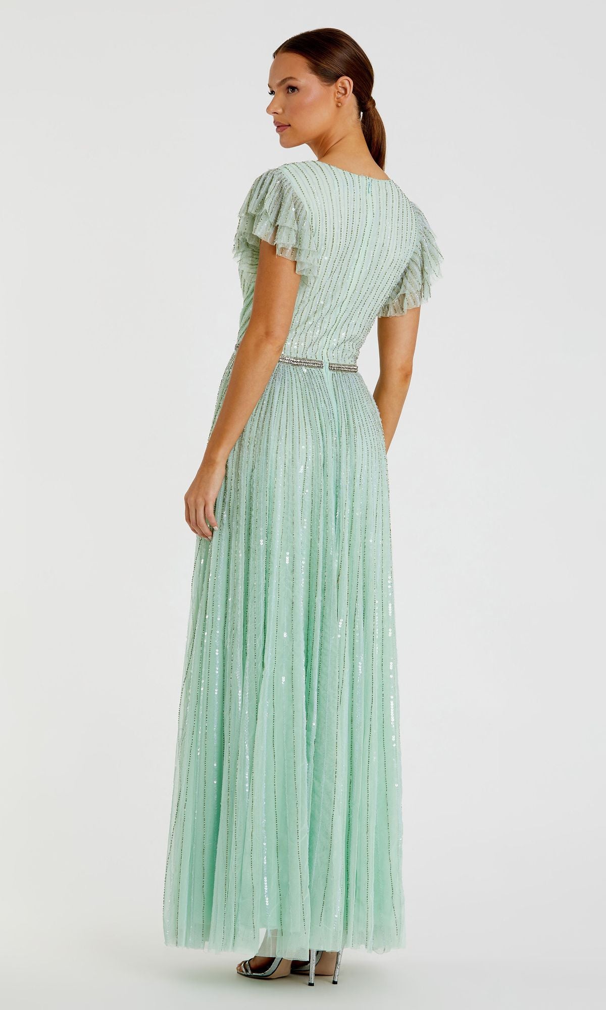 A woman models the Sequin-Stripe Long Formal Dress: Mac Duggal 5502, a floor-length light green gown with short ruffled sleeves, vertical stripes, and subtle sequins, standing and facing slightly away from the camera.
