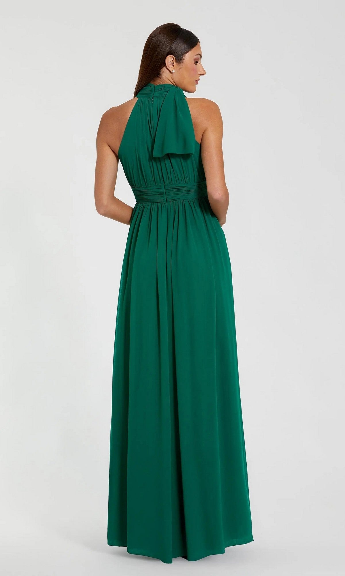 Woman stands with her back to the camera, wearing the Mac Duggal 55035 High-Neck Long Formal Dress in emerald green, featuring a sleeveless design and tied halter neck.