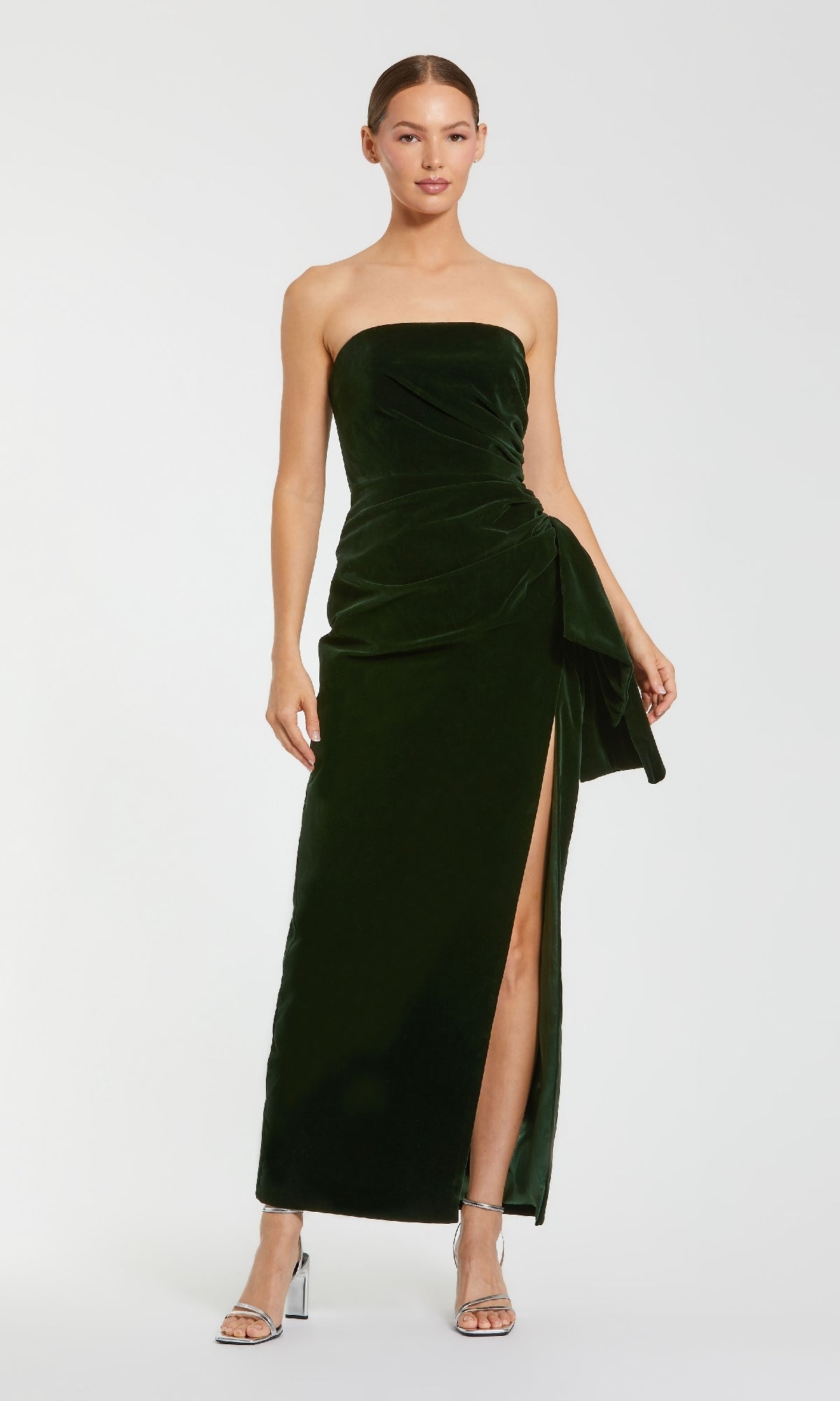 A woman models the Mac Duggal 55080 Strapless Velvet Formal Gown in dark green with a side slit, posing against a plain white background.