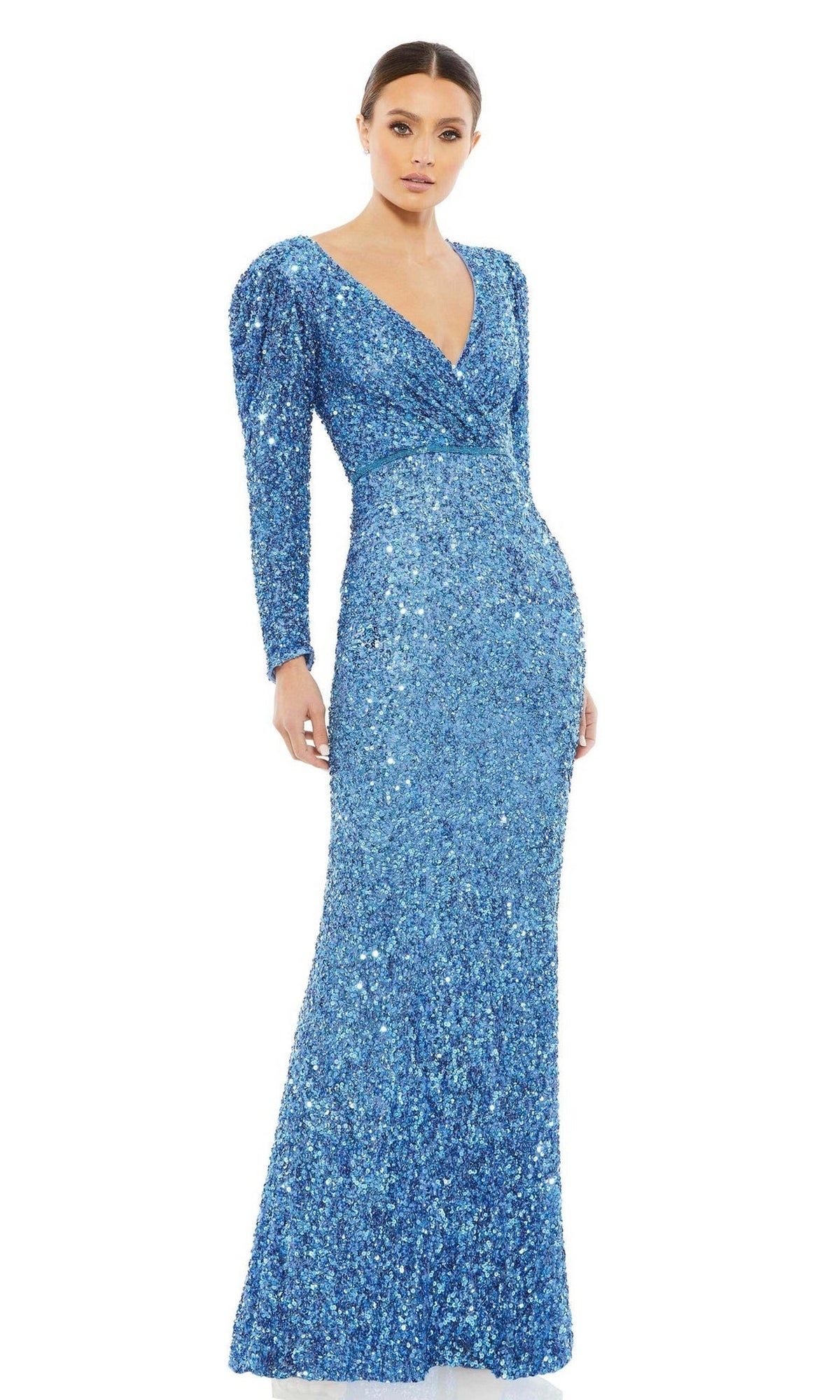 A woman models the Mac Duggal 5510 Long Sleeve Sequin Formal Dress, a fitted blue gown with a deep V-neckline, standing against a plain white background.