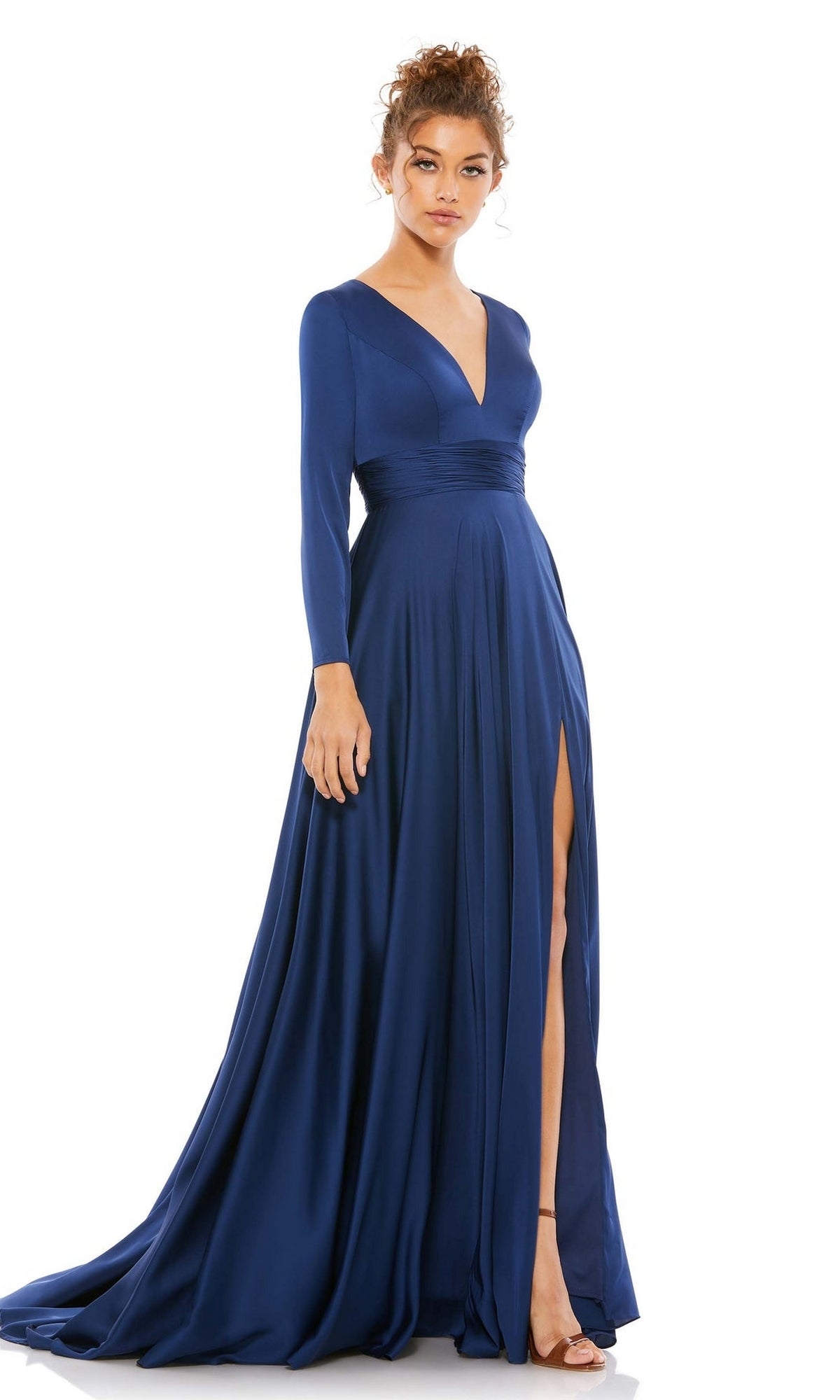 A woman wearing the Mac Duggal 55245 Long Sleeve Long Formal Dress—a deep blue A-line gown with a fitted waist, deep V-neck, and high slit—stands against a white background.
