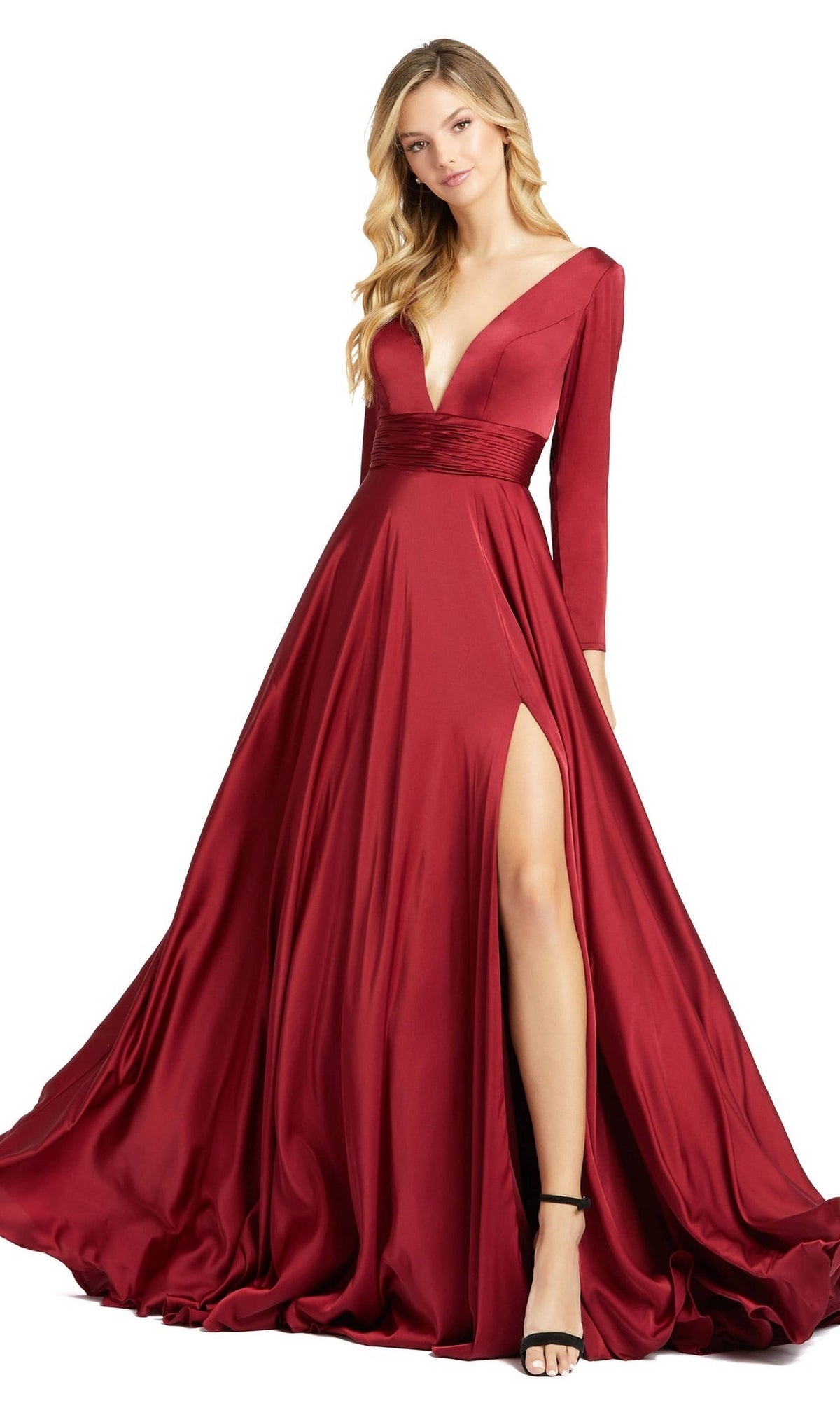 A woman wears the Mac Duggal 55245 Long Sleeve Long Formal Dress in deep red satin with a deep V-neck, fitted waist, and high leg slit, styled elegantly with black high-heeled sandals.