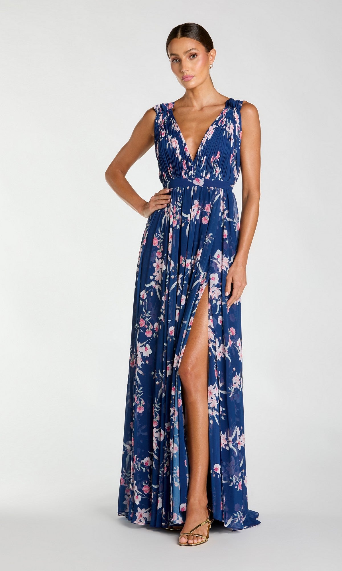 A woman models the Mac Duggal 55321 Classic Long Formal Dress—sleeveless, deep V-neck, floor-length, blue floral with a high slit—standing neutrally against a plain background.