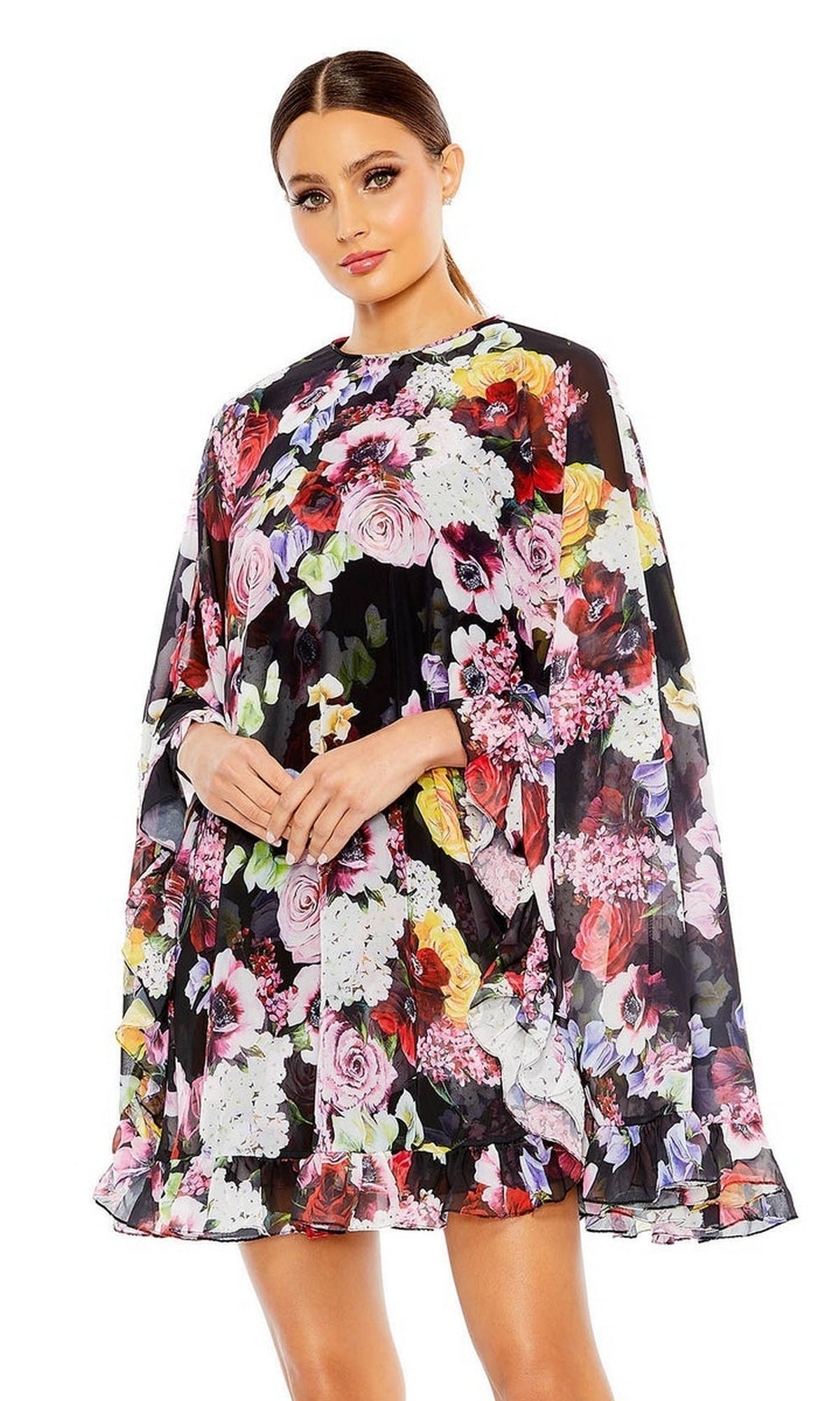 A woman wears the Mac Duggal 55404 Short Print Cape Hoco Dress, featuring a loose fit and floral print, standing against a white background.