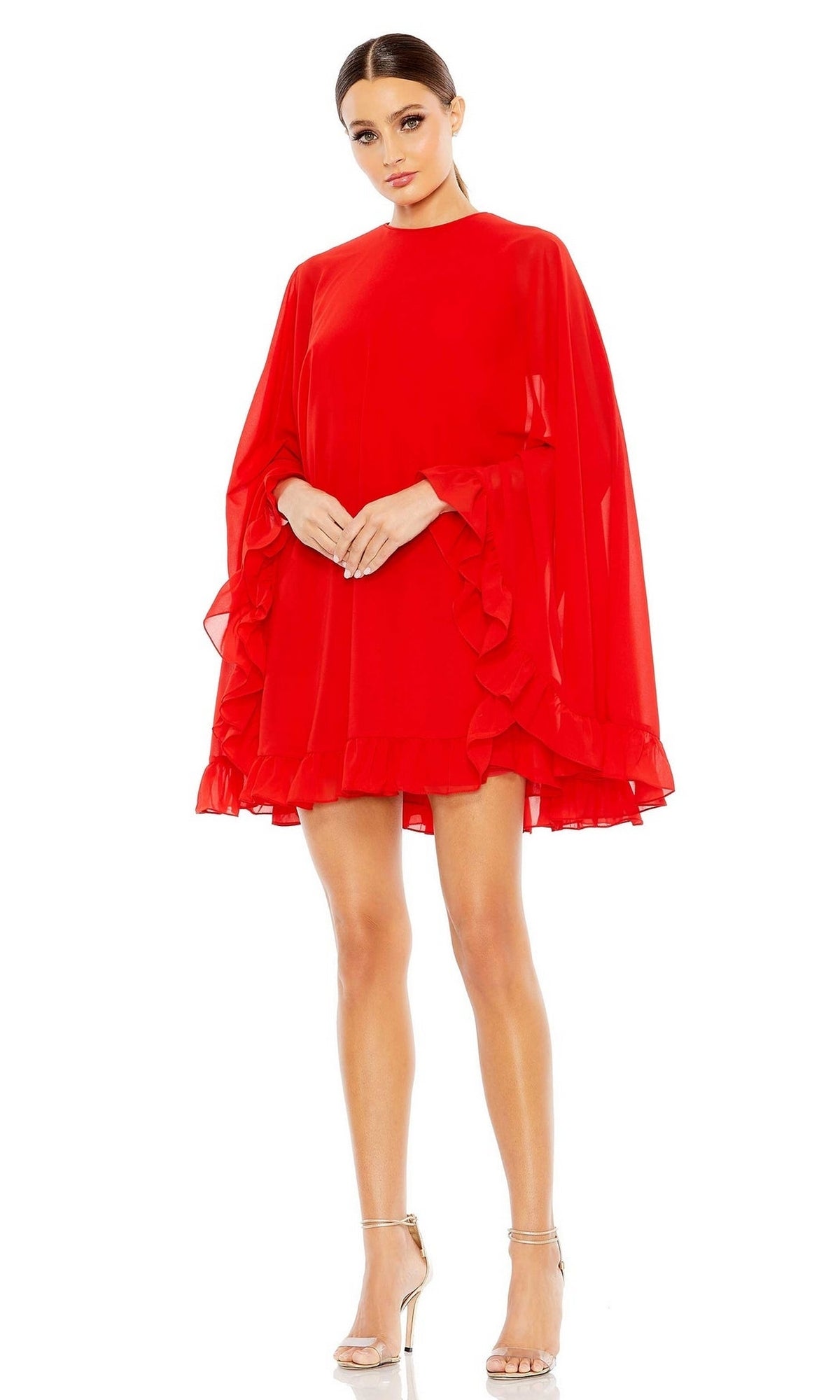 A woman stands against a white background, wearing the Long Sleeve Short Red Dress 554071 by Mac Duggal with ruffle and cape sleeve details, paired with silver high-heeled sandals.
