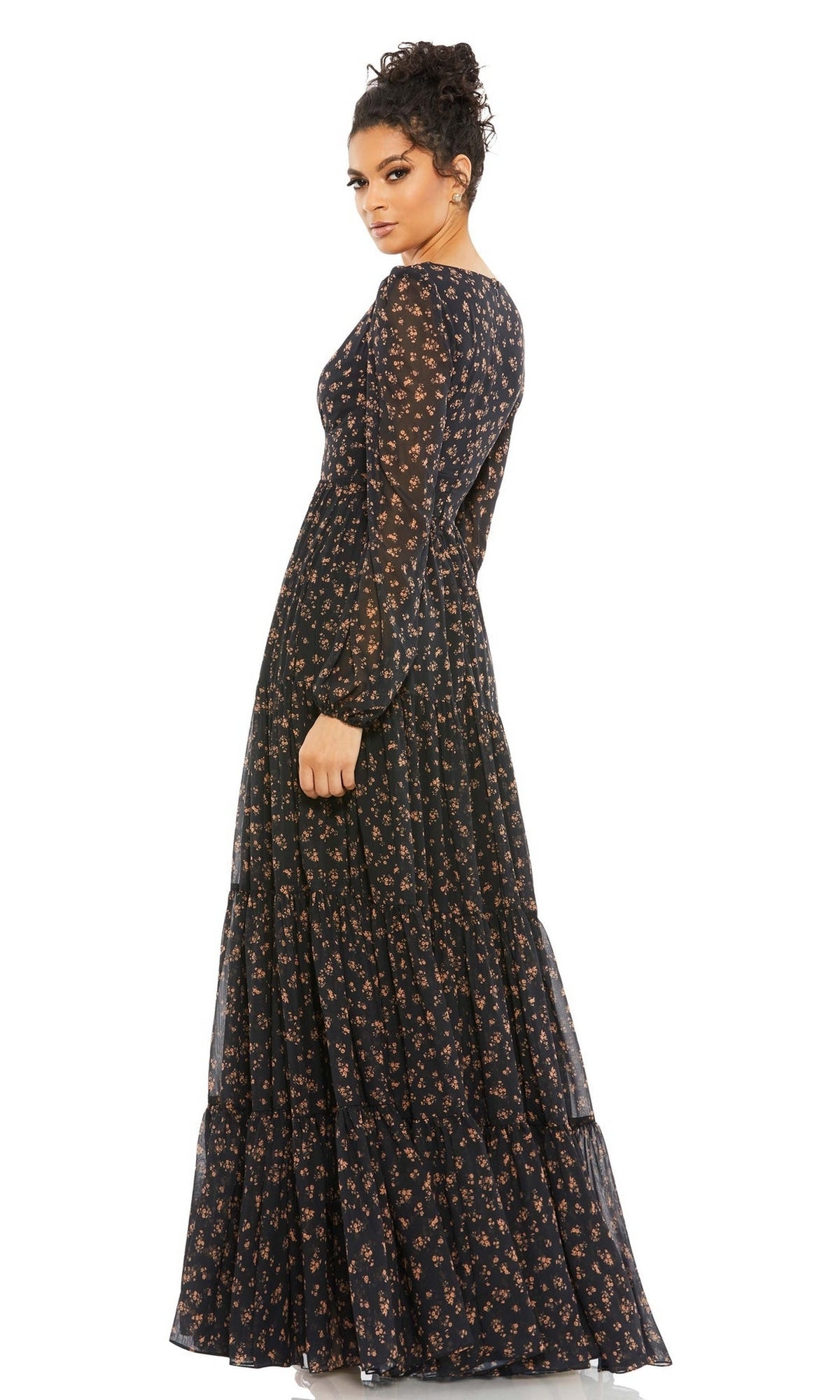 A person models the Long Formal Dress 55431 by Mac Duggal, a black floor-length v-neck gown with sheer long sleeves, a tiered skirt, and an elegant floral print, set against a white background.