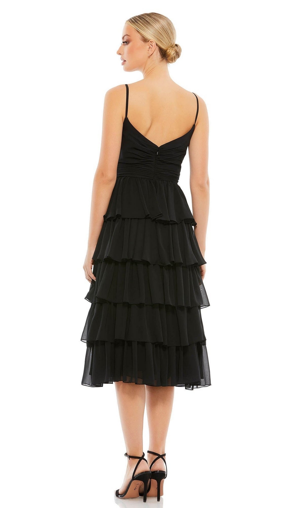 Woman facing away in the Mac Duggal 55437 Black Midi Wedding Guest Dress, featuring spaghetti straps and black high-heeled sandals. Her hair is styled in a neat low bun for a chic, elegant look.