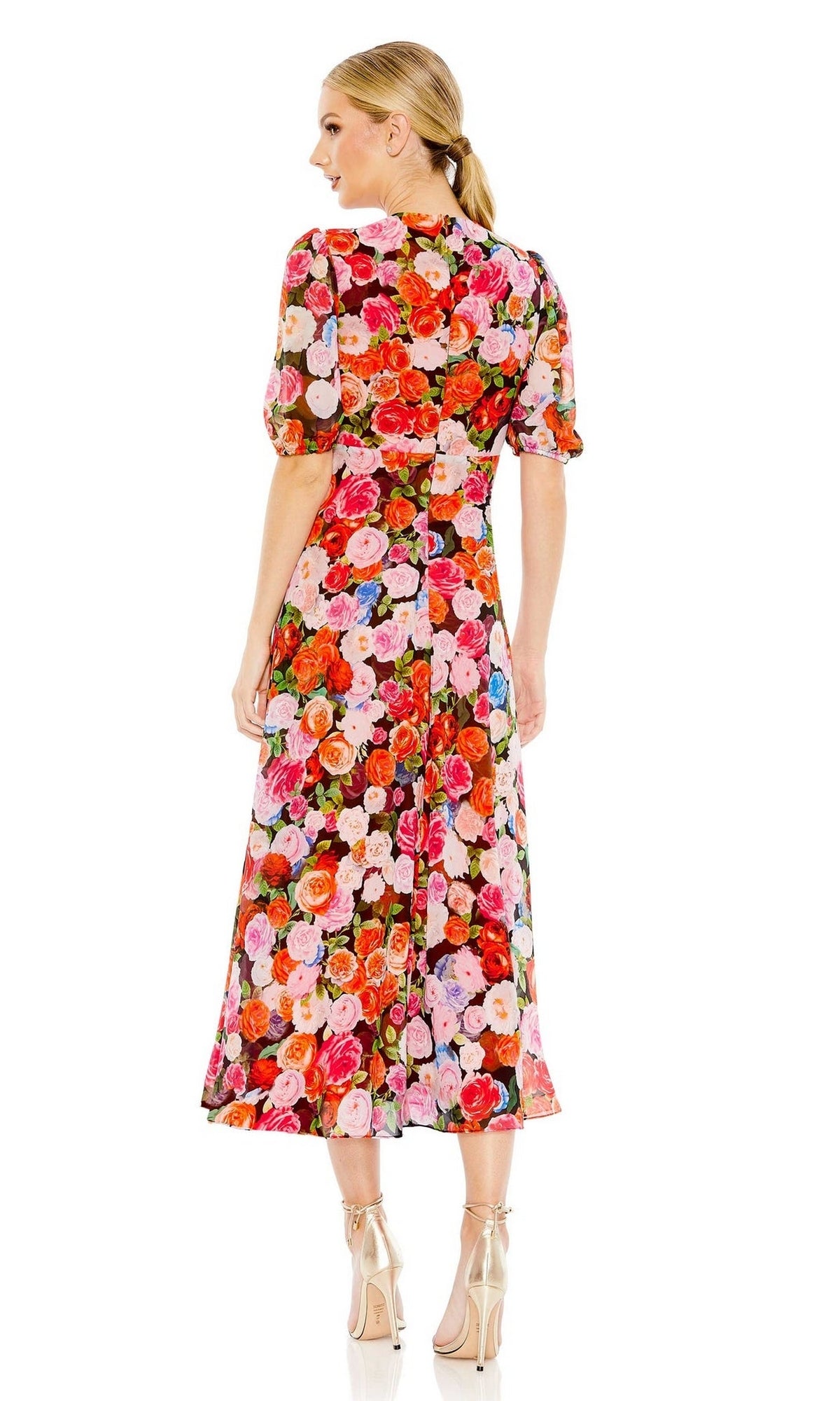 A woman faces away, wearing the Mac Duggal 55626 Short Sleeve Midi Print Party Dress with pink, red, and orange rose patterns, paired with nude high heels.