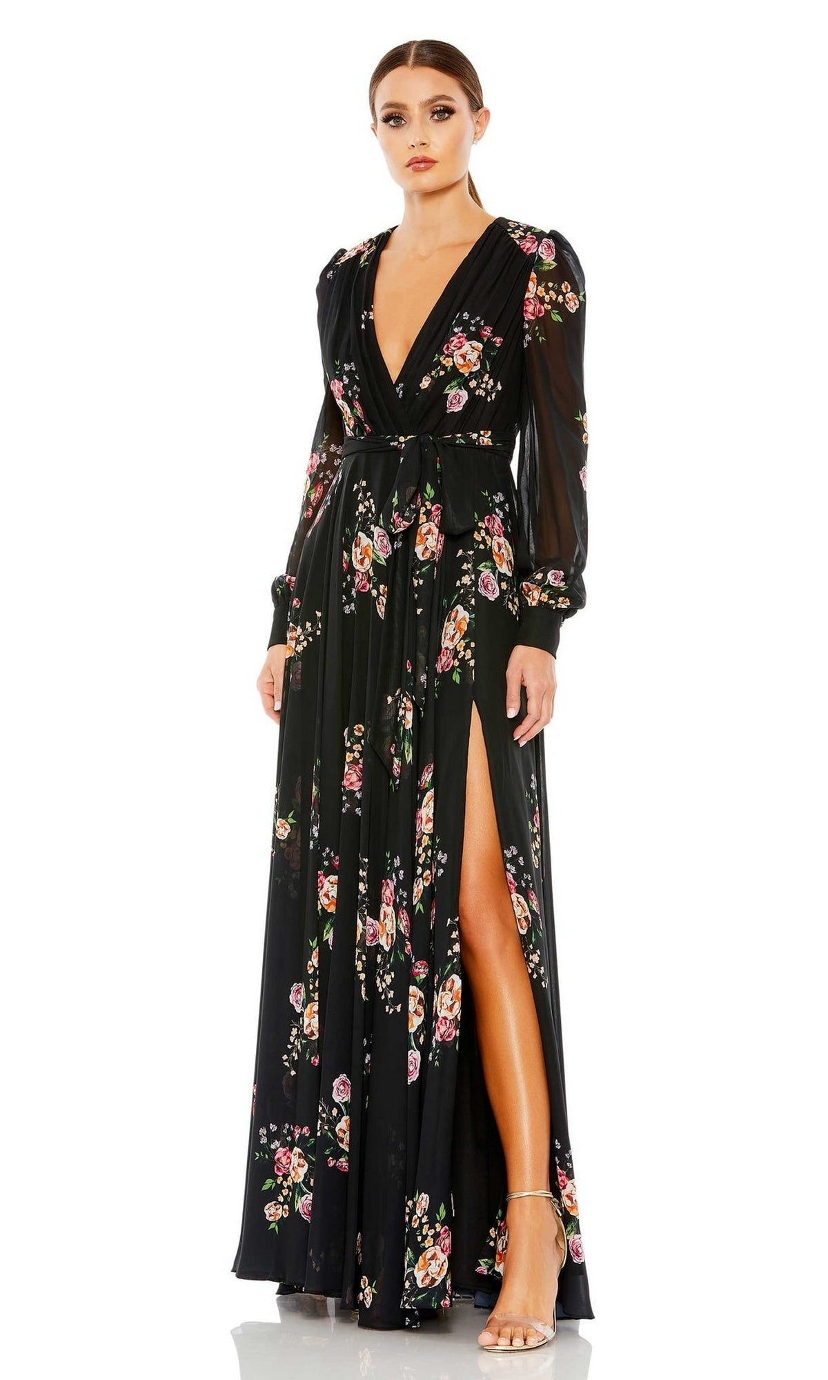 A woman in the Mac Duggal 55661 long black print formal dress with long sleeves, a deep V-neckline, and thigh-high slit stands in heels against a white background.