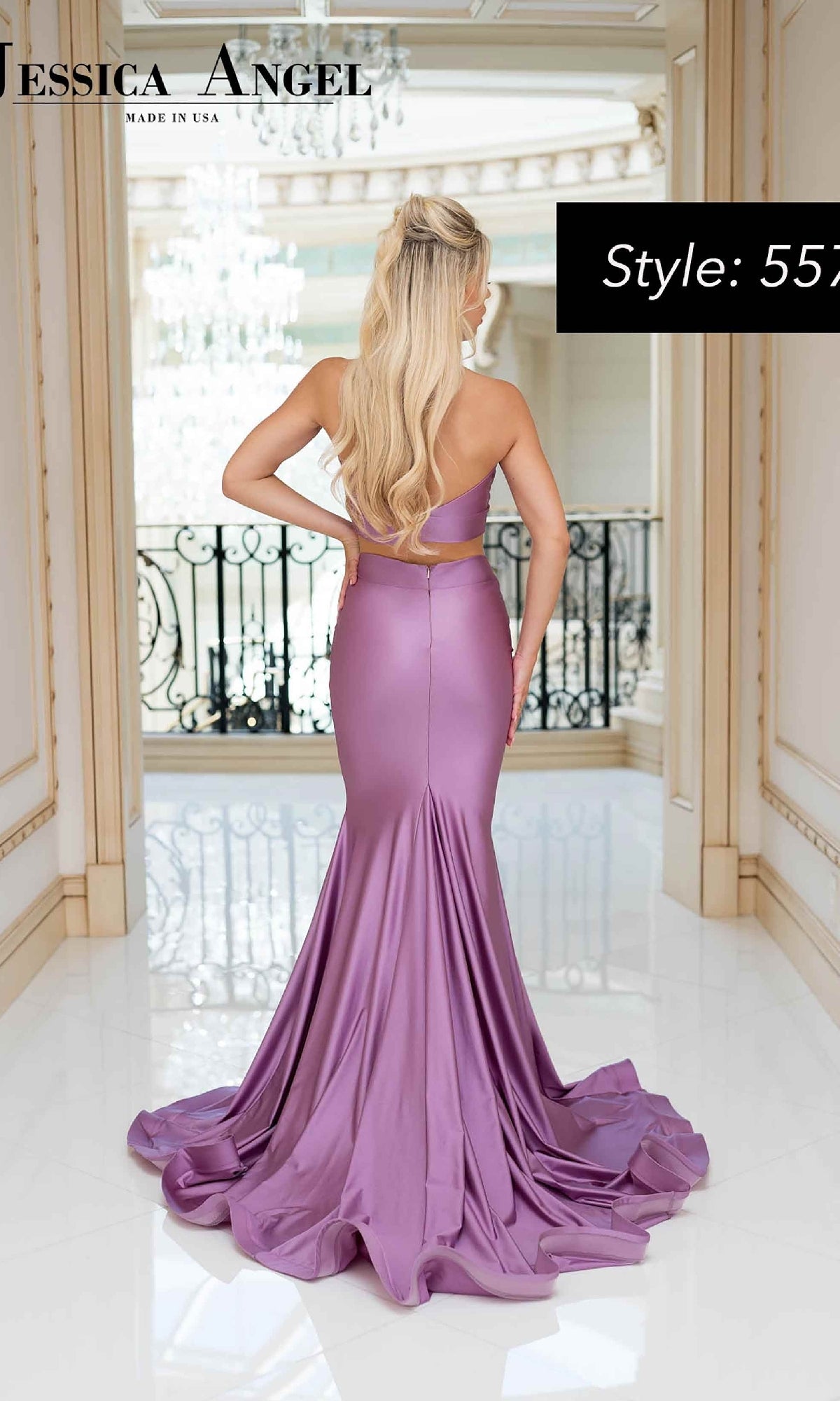 Woman in a two-piece halter Jessica Angel 557 prom gown stands indoors, facing away. The fitted lavender dress has a train and cutout back, with a chandelier and decorative railing visible in the background.