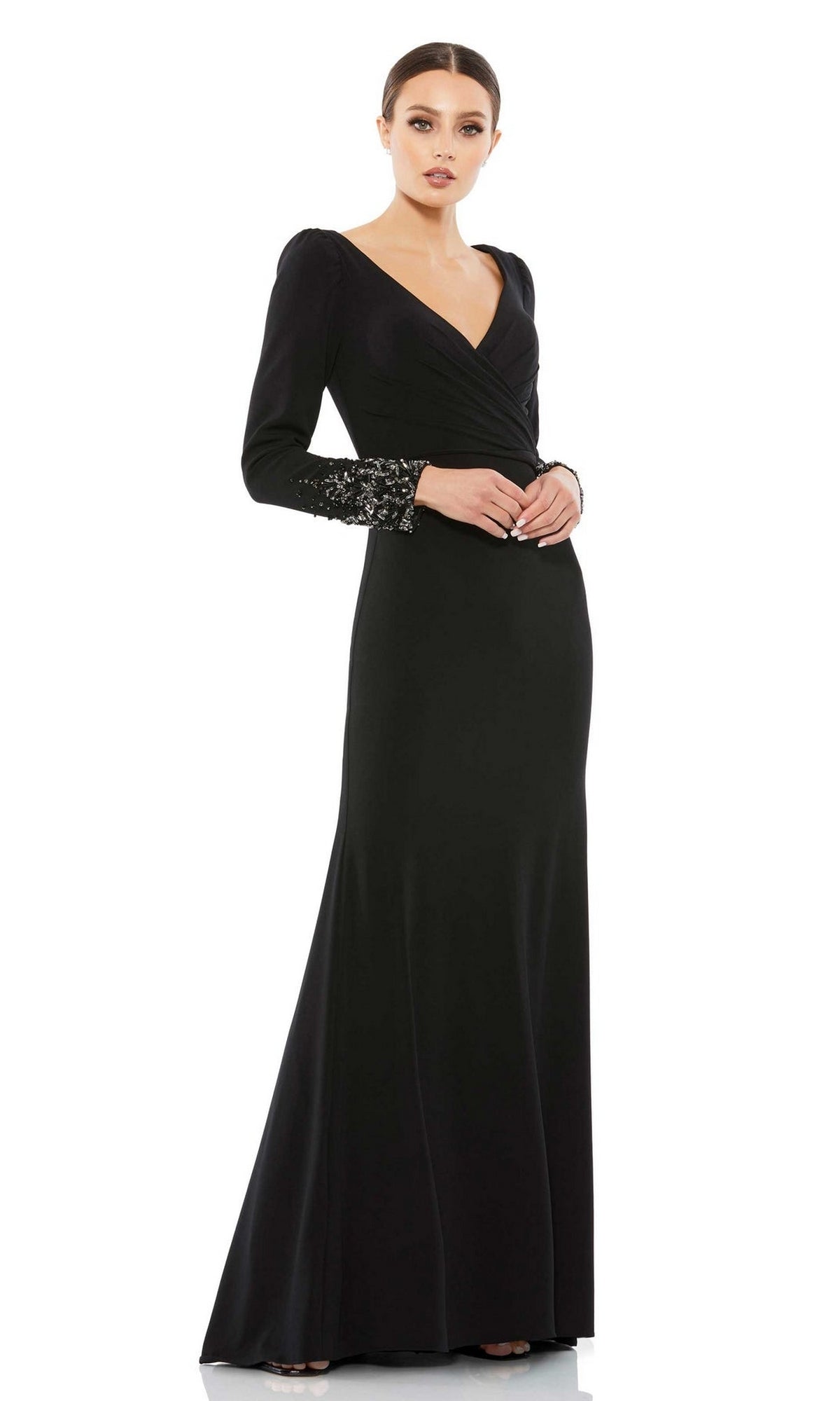 A woman wears the Mac Duggal Long Formal Dress 55712, featuring long sleeves and elegant lace-detailed cuffs, standing with her hands clasped and looking at the camera.