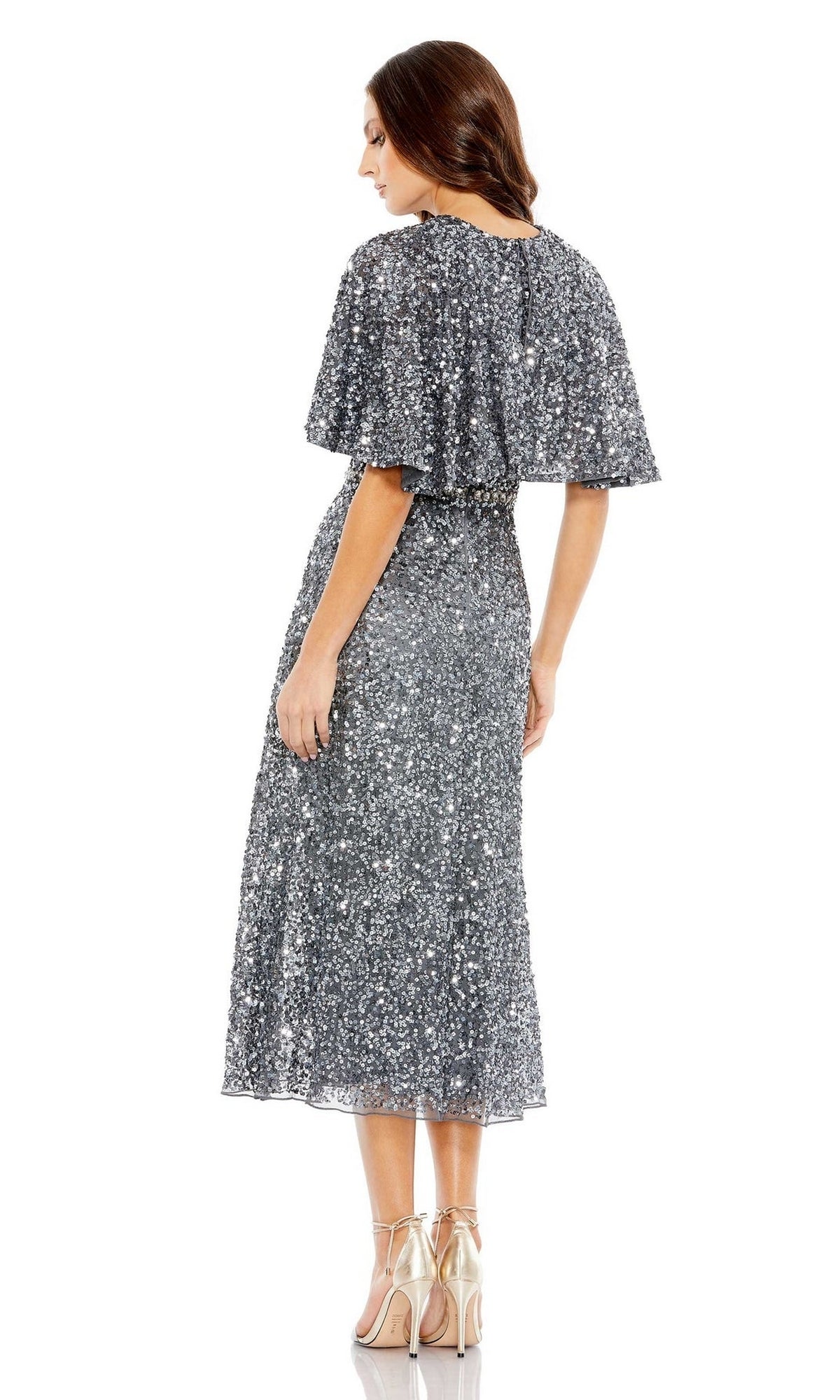 A woman stands facing away against a white background, wearing the Mac Duggal 5577 Caped Midi Semi-Formal Dress in silver sequins with short flutter sleeves, paired with metallic high-heeled sandals.