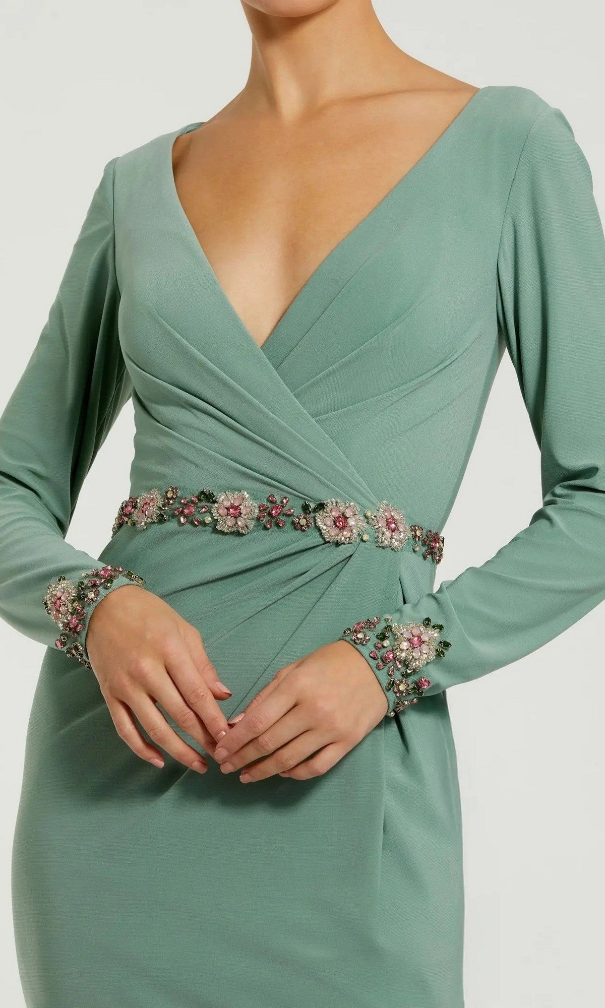 Wearing the Mac Duggal 55784, a sage green long formal dress featuring long sleeves, a deep V-neckline, and a floral beaded waistband accentuating both the waist and cuffs. This elegant piece exudes the timeless sophistication characteristic of Mac Duggal designs.