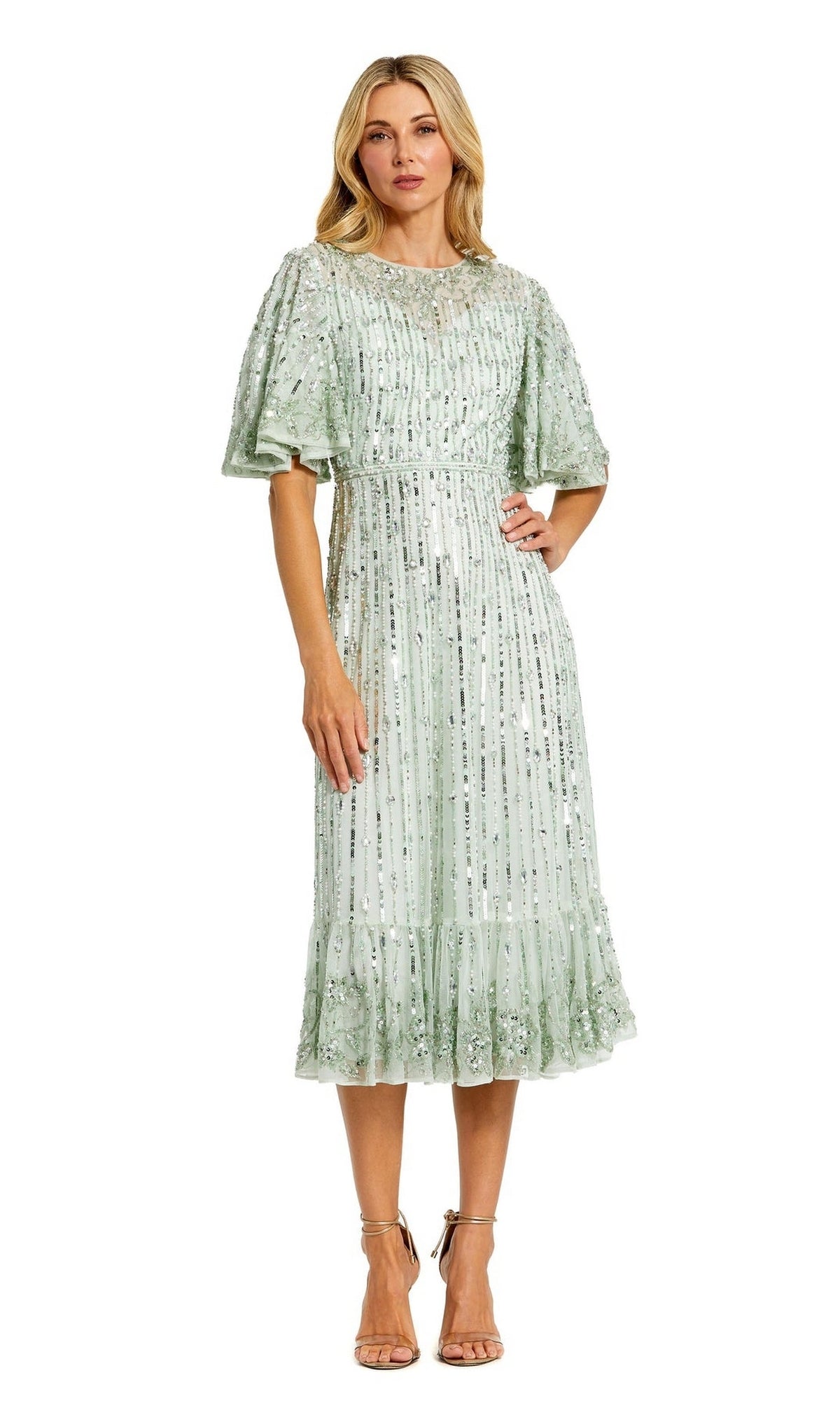A woman wears the Mac Duggal 5579 Beaded Midi Semi-Formal Dress in light green, featuring sequin embellishments and a ruffled hem, styled with nude strappy heels for a chic semi-formal look.