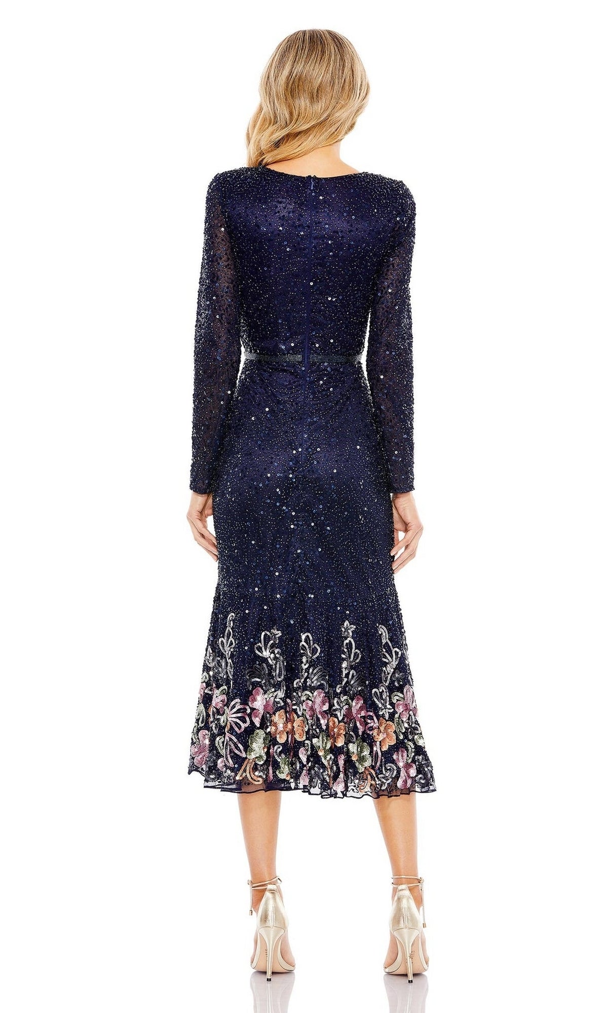 A woman stands in high heels, seen from the back, wearing the Mac Duggal 5589 Beaded Midi Wedding Guest Dress in navy blue with long sleeves and floral embroidery at the hem.