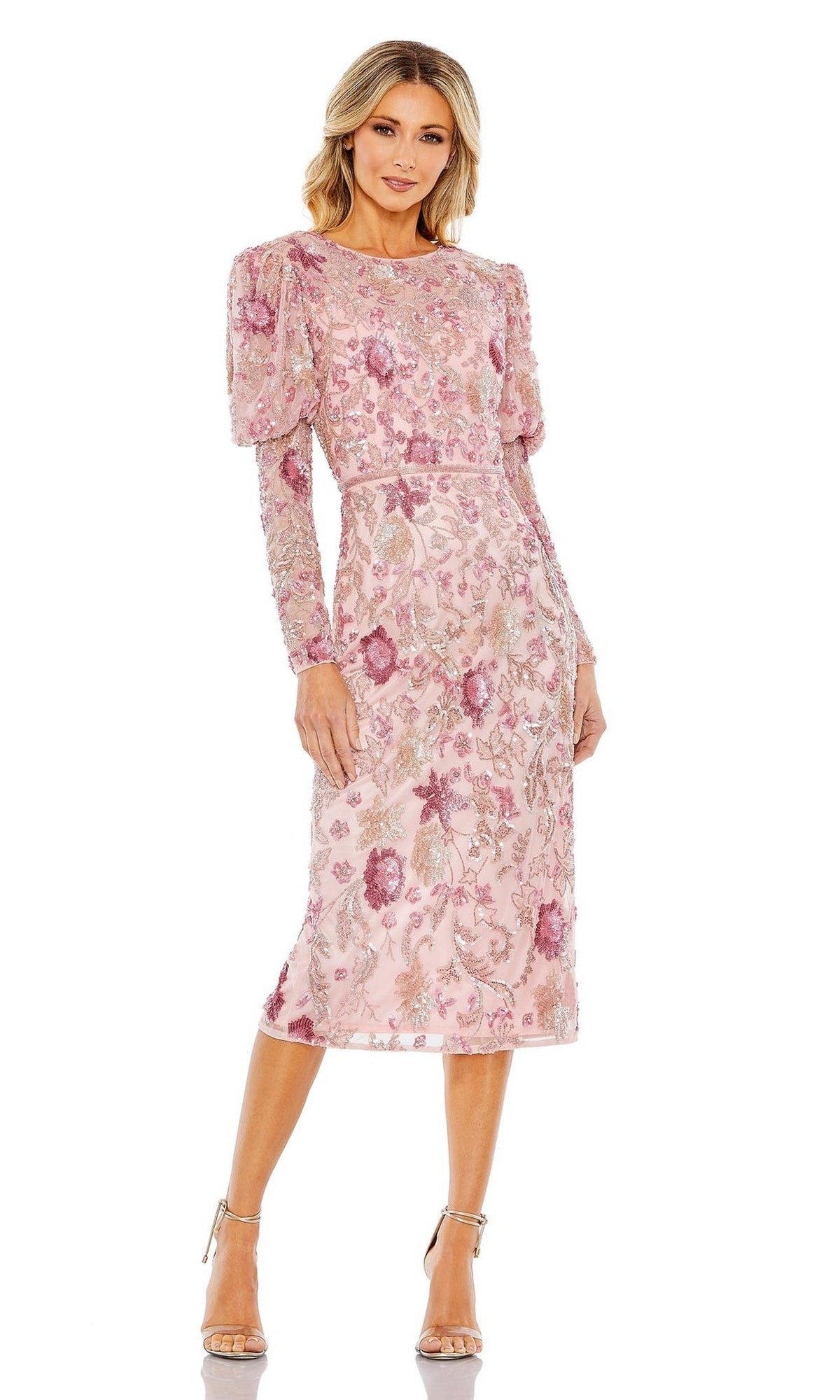 A woman in the Short Semi-Formal Dress 5590 by Mac Duggal—pink, floral embroidered, long-sleeve with a beaded waistband—pairs it with nude high-heeled sandals while standing against a white background.