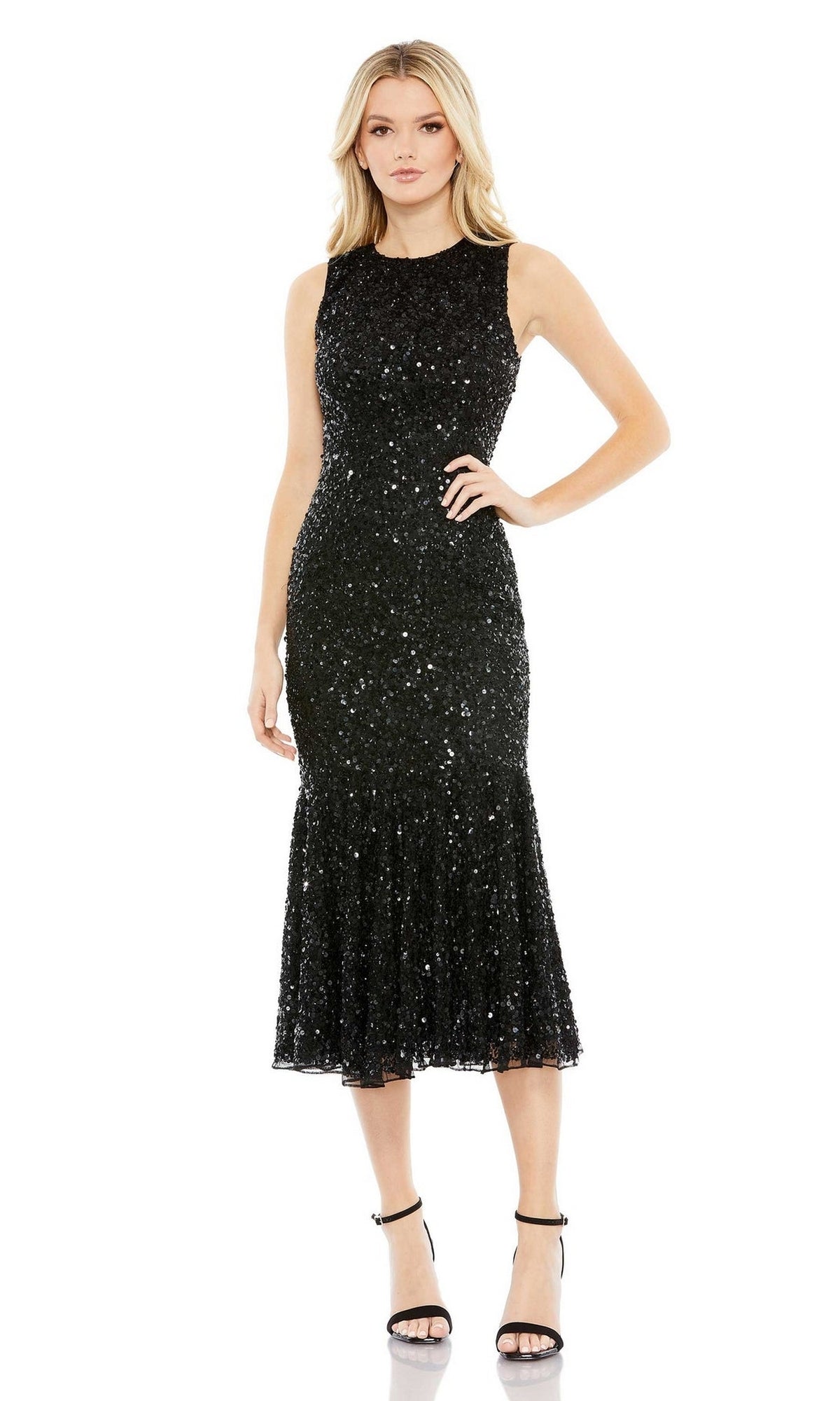 A woman models the Short Semi-Formal Dress 5597 by Mac Duggal—a sleeveless, fitted black midi dress with sequins and a flared hem—styled with black ankle-strap heels for elegant evenings against a white background.