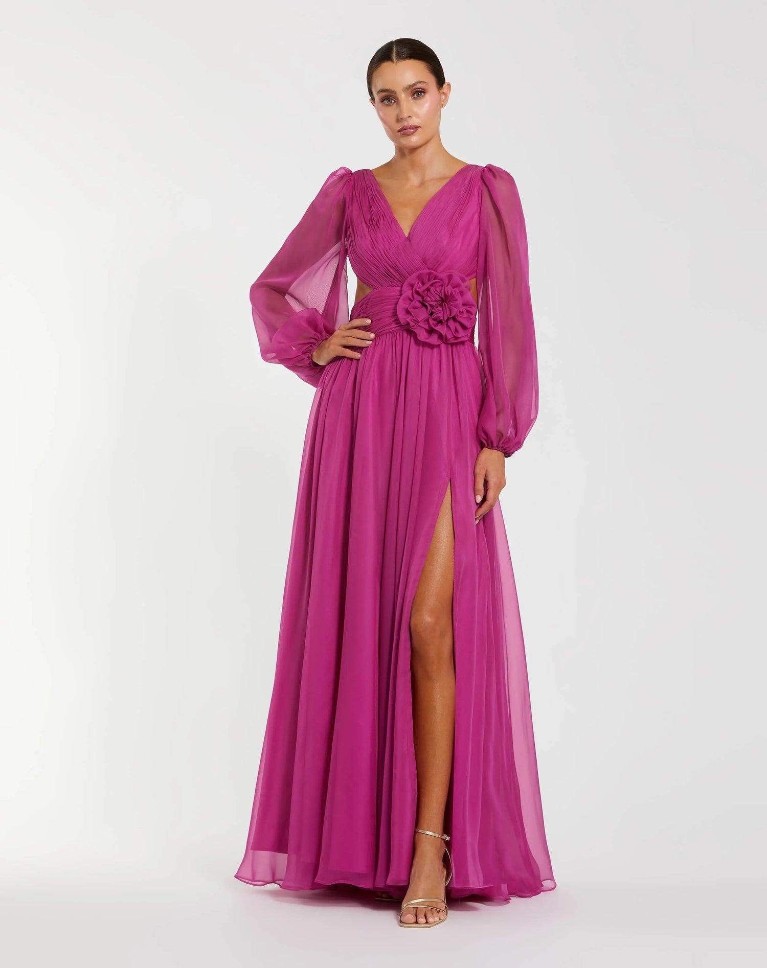 A woman wears the Long Formal Dress: Mac Duggal 56072 in magenta, featuring sheer long bishop sleeves, a V-neckline, a floral waist detail, and a high front slit. She stands against a plain light background.