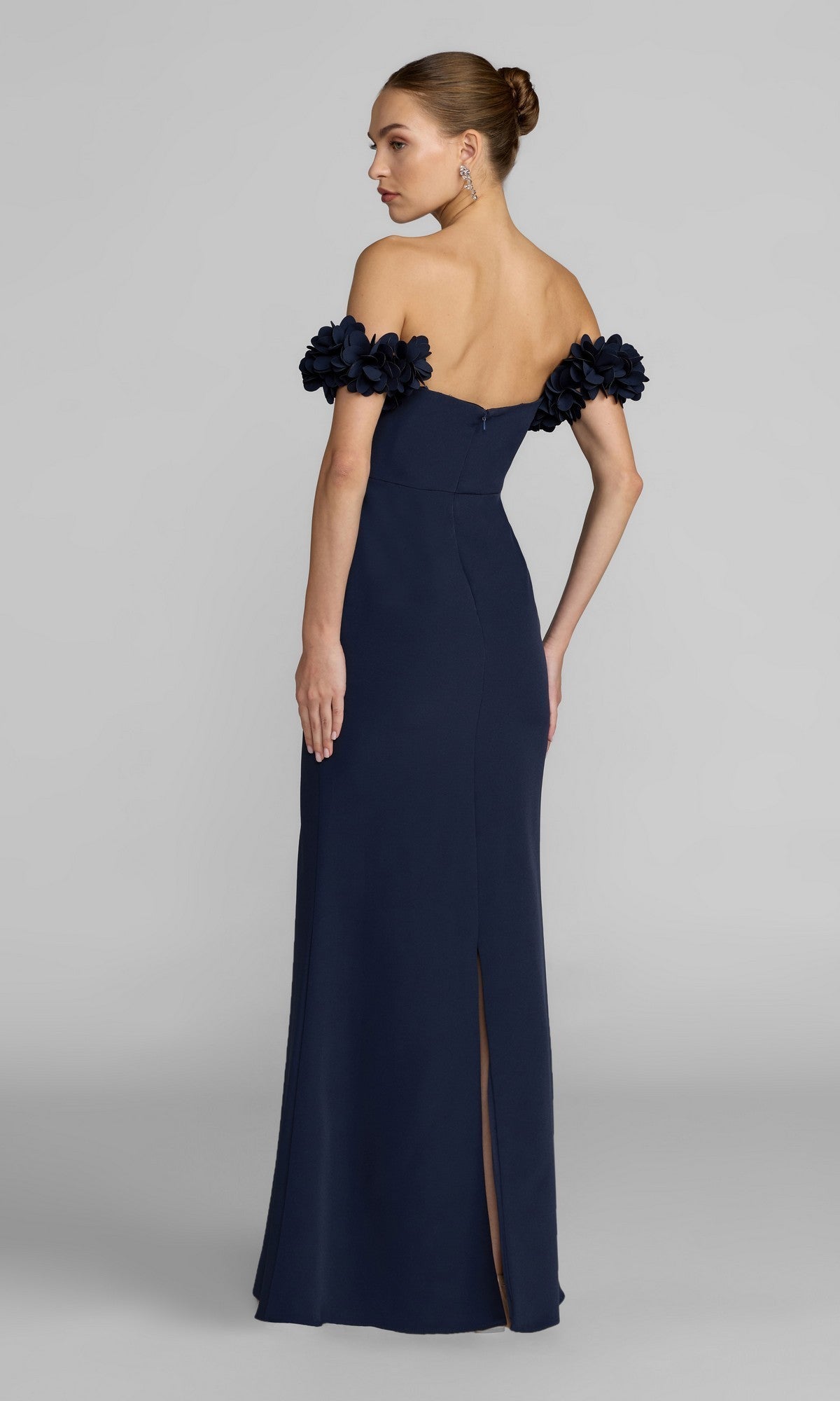 A woman stands with her back to the camera, wearing the Mac Duggal 56131 Floral-Straps Long Formal Dress in navy blue—a graceful off-the-shoulder crepe gown with floral sleeve details, ideal for refined special occasions.