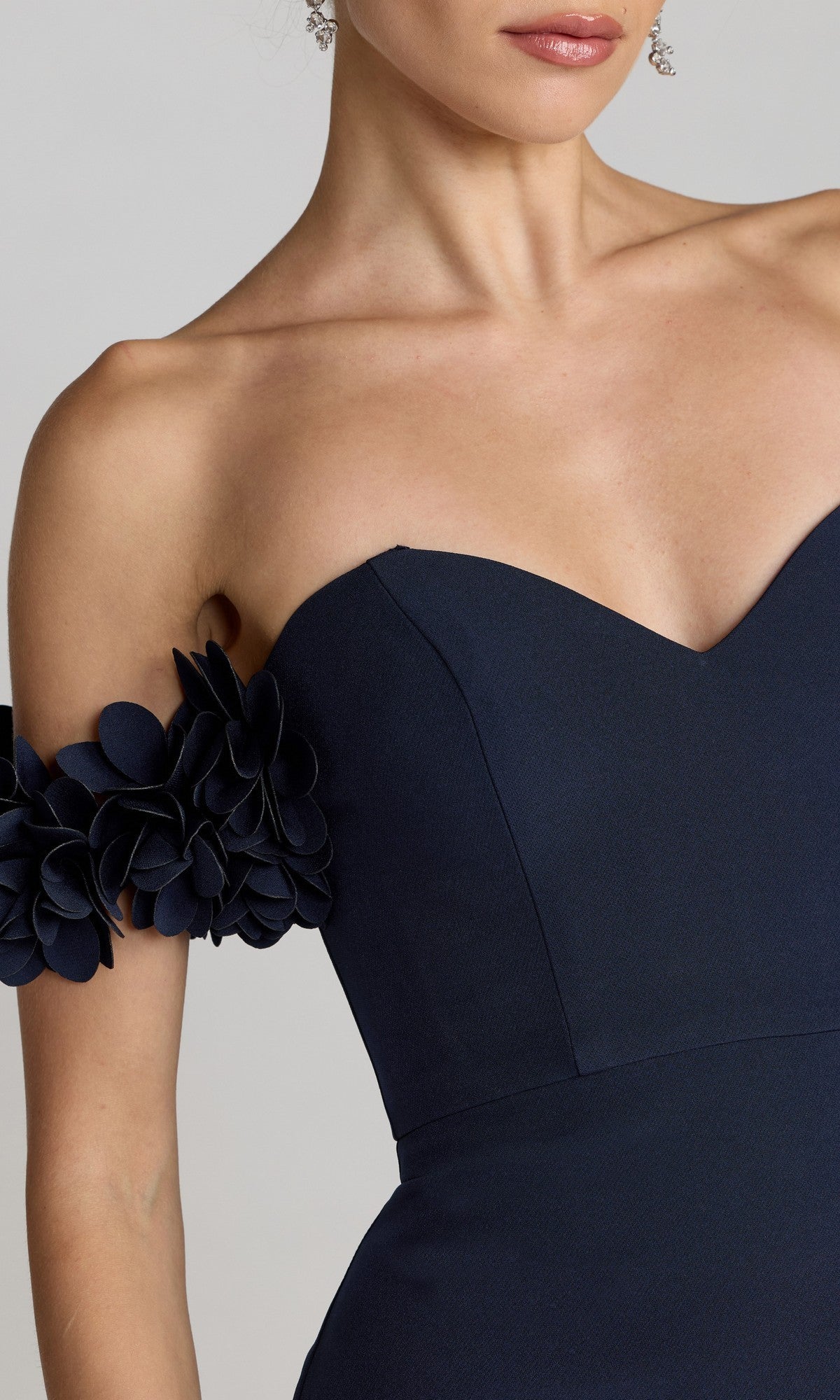 A woman wears the Mac Duggal 56131 Floral-Straps Long Formal Dress, a fitted navy evening gown with floral strap details, shown from shoulders to waist.