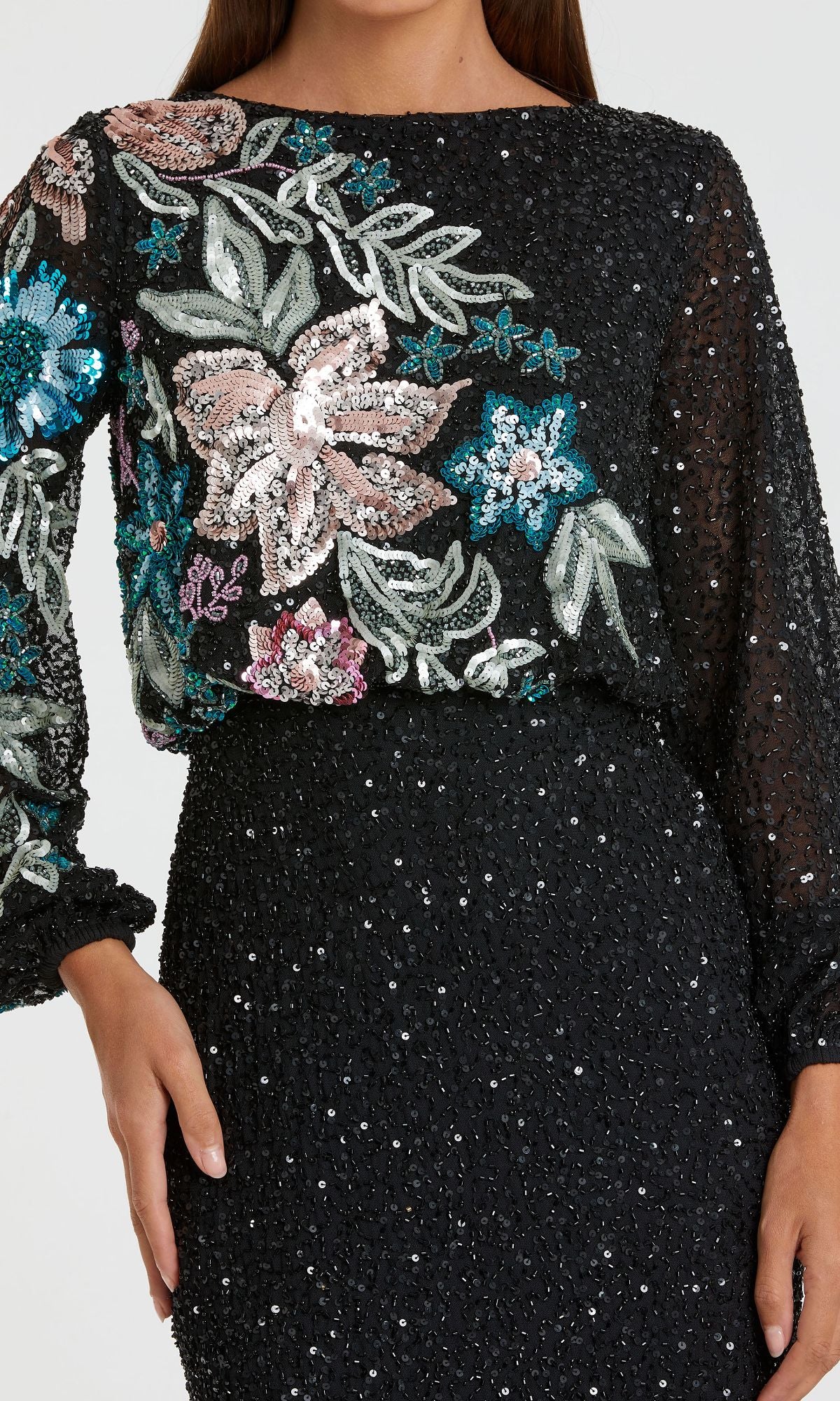 A woman wears the Mac Duggal 5615 Beaded Long Sleeve Formal Dress—a black gown with sequin embellishments and vibrant embroidered floral details on the bodice.