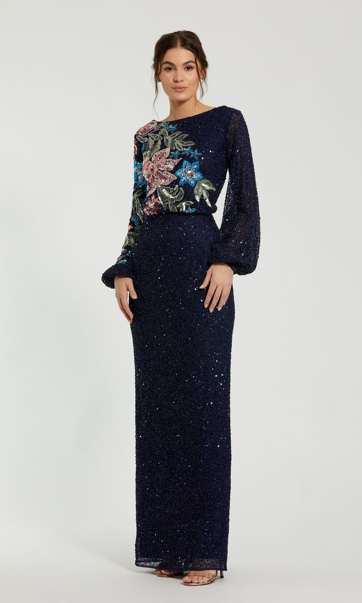 A woman wears the Mac Duggal 5615 Beaded Long Sleeve Formal Dress, featuring navy blue fabric with glitter, beading, and floral embroidery on the sleeves and upper bodice, set against a plain light background.