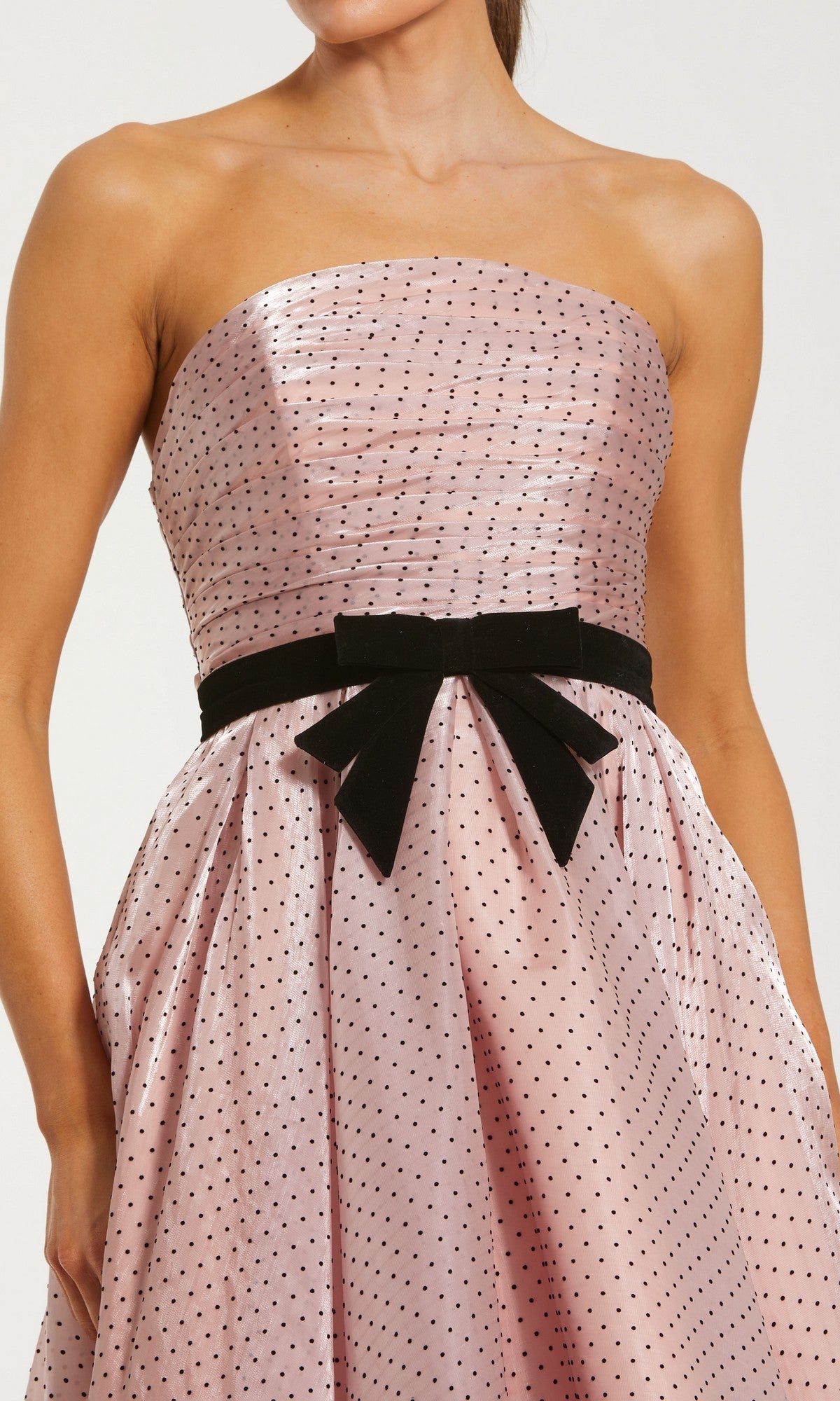 A woman wearing the Mac Duggal 56184 long formal dress: a strapless organza gown in light pink with black polka dots, featuring a fitted bodice and accented with a black velvet bow at the waist.