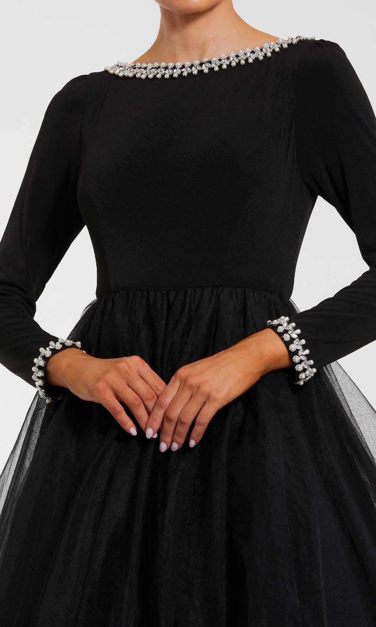 A woman in the Mac Duggal 56186 long sleeve black formal gown with pearl-embellished collar and cuffs stands with her hands clasped.